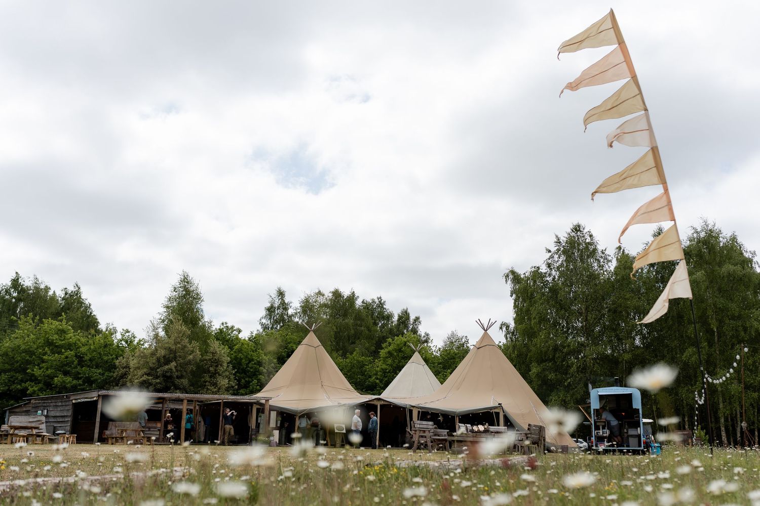 A scenic outdoor wedding venue with Nordic tipis and bunting flags against a cloudy sky.