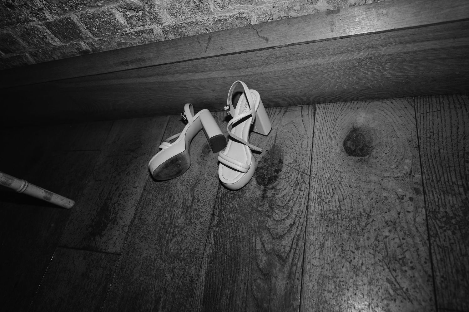 Black and white photo of bridal heels left on a wooden floor at a wedding.