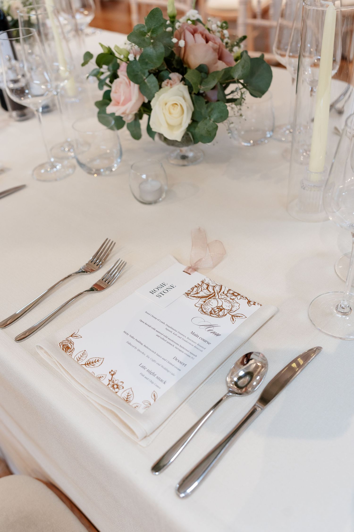 Elegant wedding table setting with floral centerpiece, menu card, and crystal glassware on white linen.