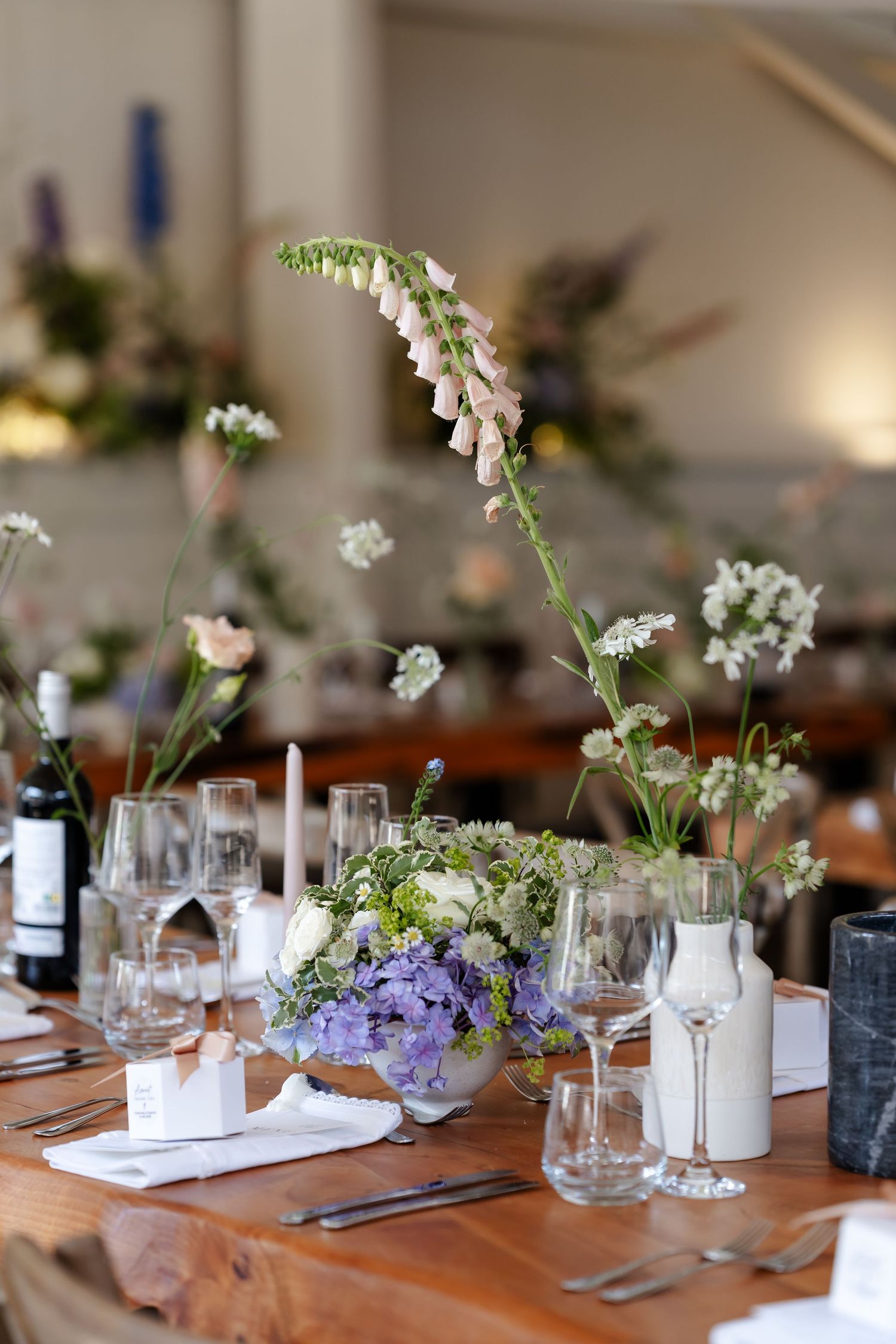 Wildflower wedding table centerpiece with foxglove, hydrangea, and white blooms on rustic wooden table.