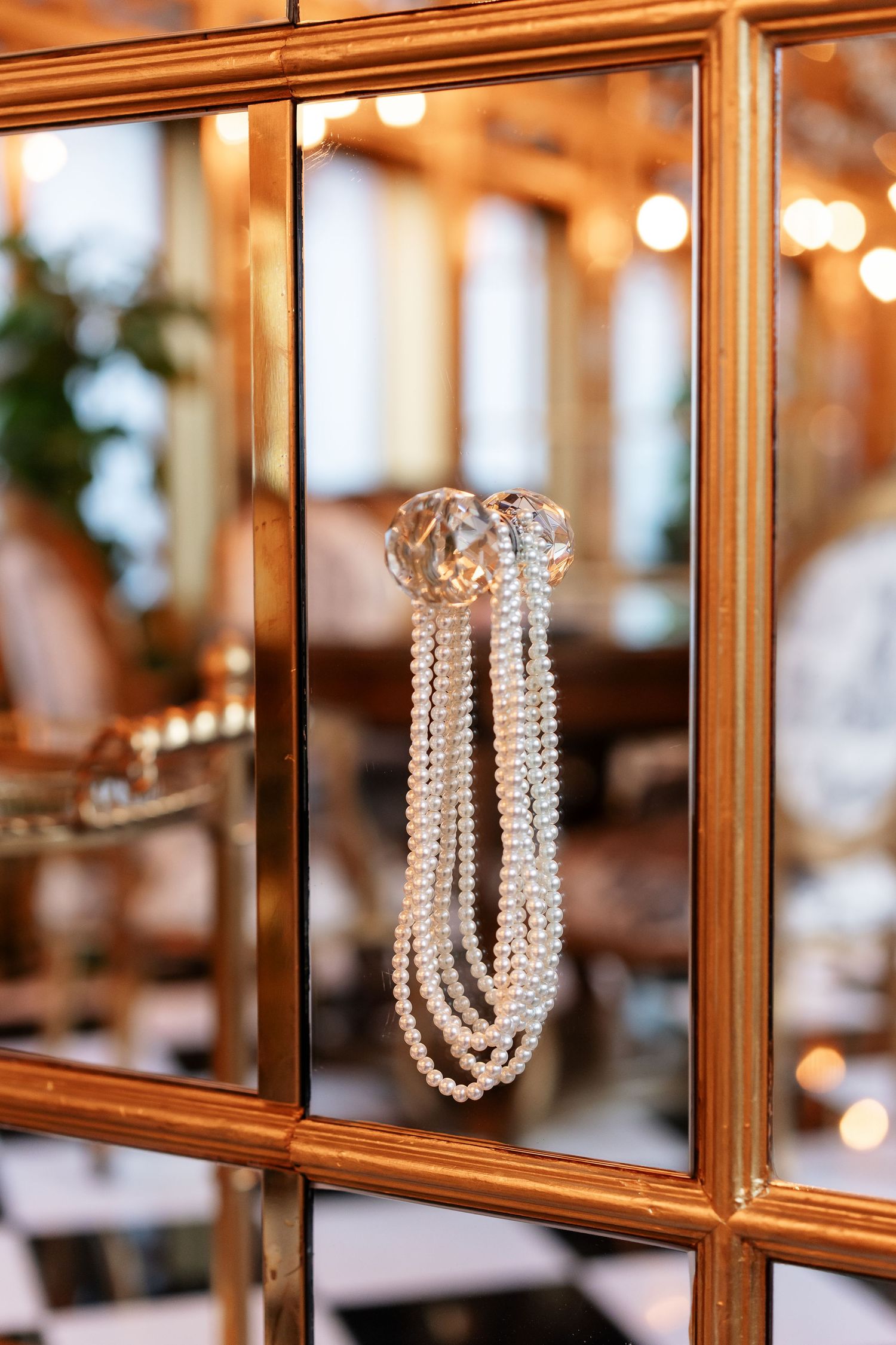 Pearl necklace draped over a crystal knob on a gold-framed mirror in elegant venue.