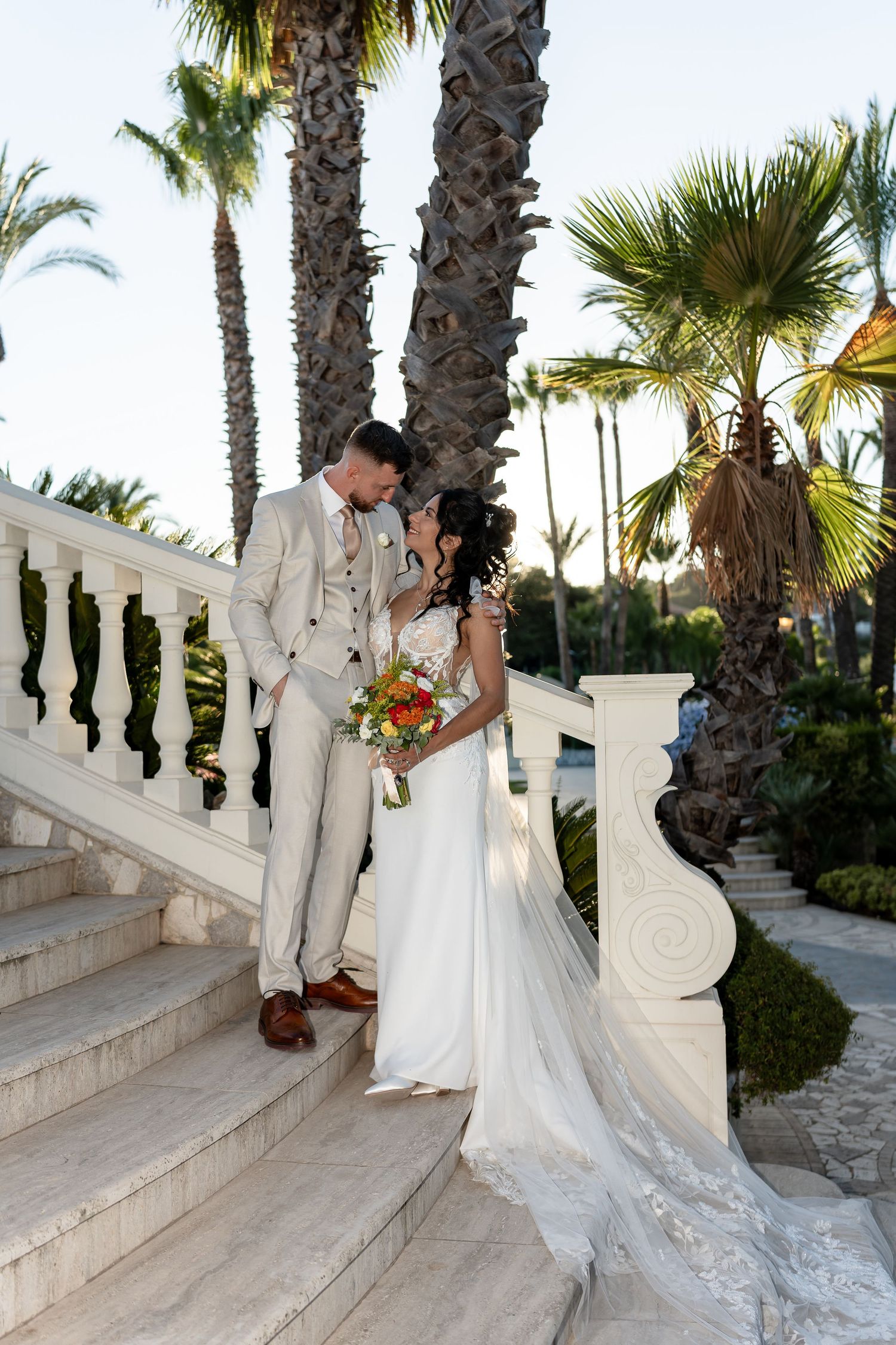 Bride and groom sharing a romantic moment on marble steps surrounded by tall palm trees.