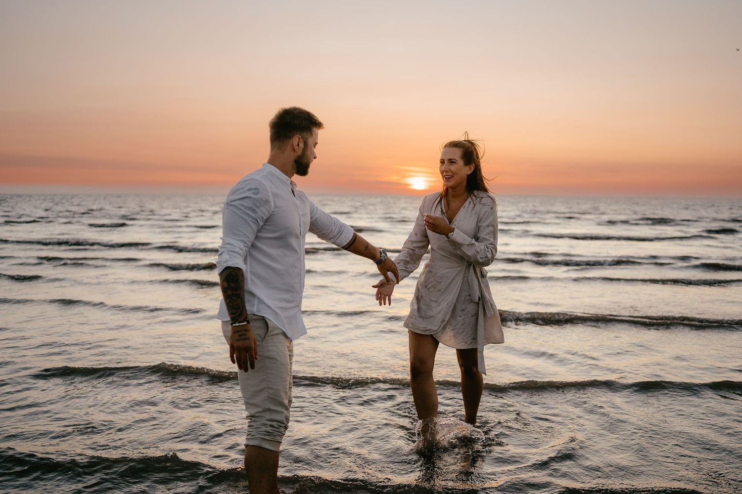 Happy couple holding hands in ocean water during romantic beach sunset.