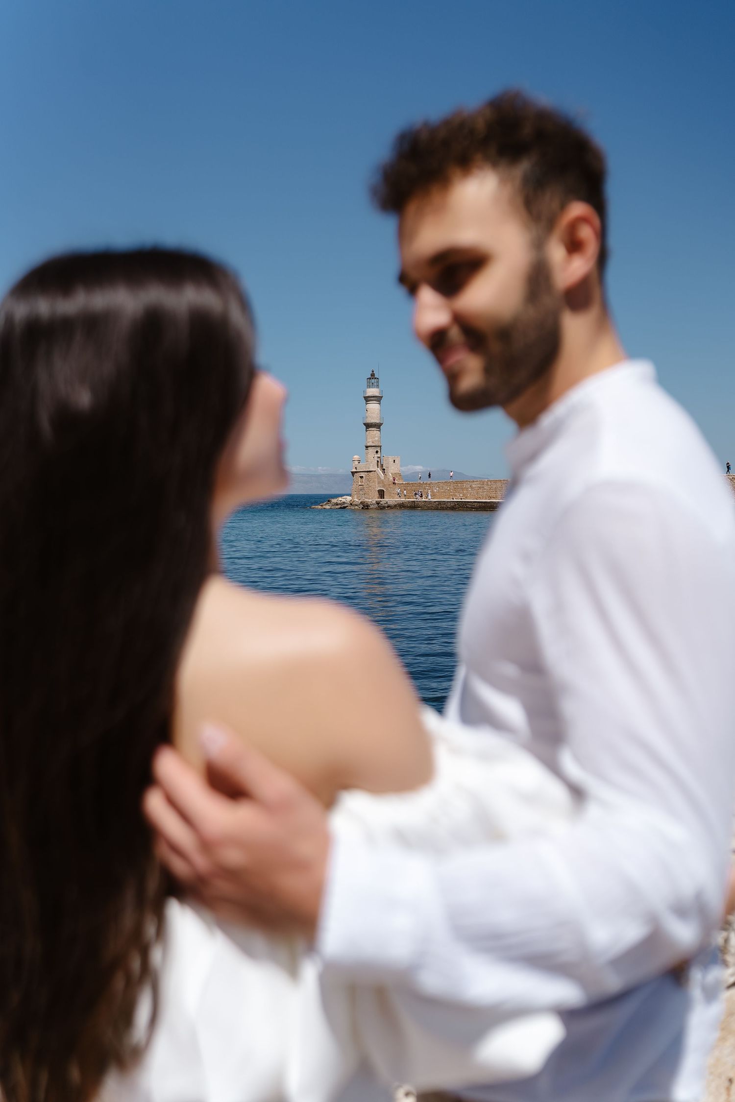 Romantic couple embracing with the iconic Chania lighthouse visible in the background in Crete.