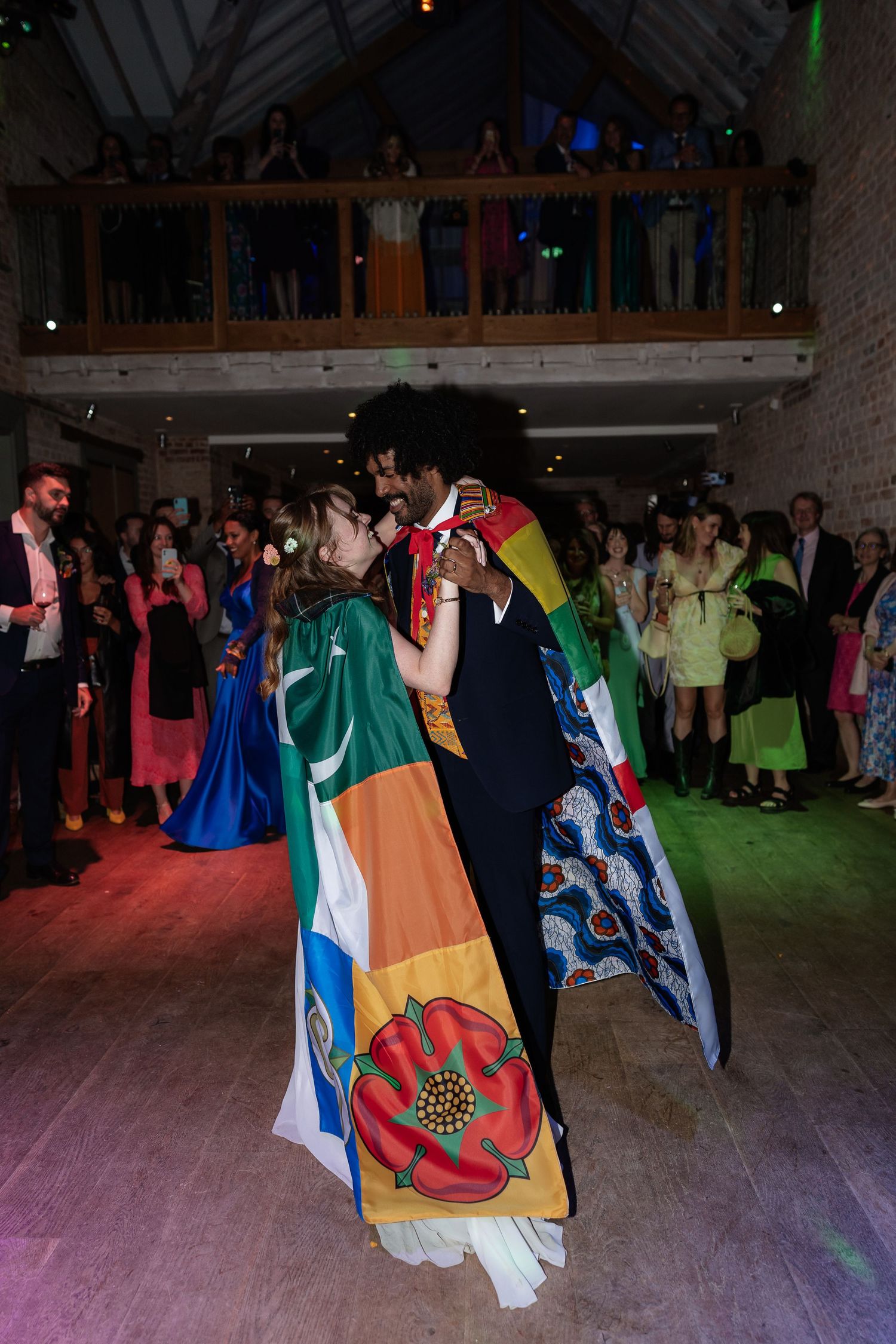Newlyweds wrapped in international flags share first dance before cheering wedding guests.