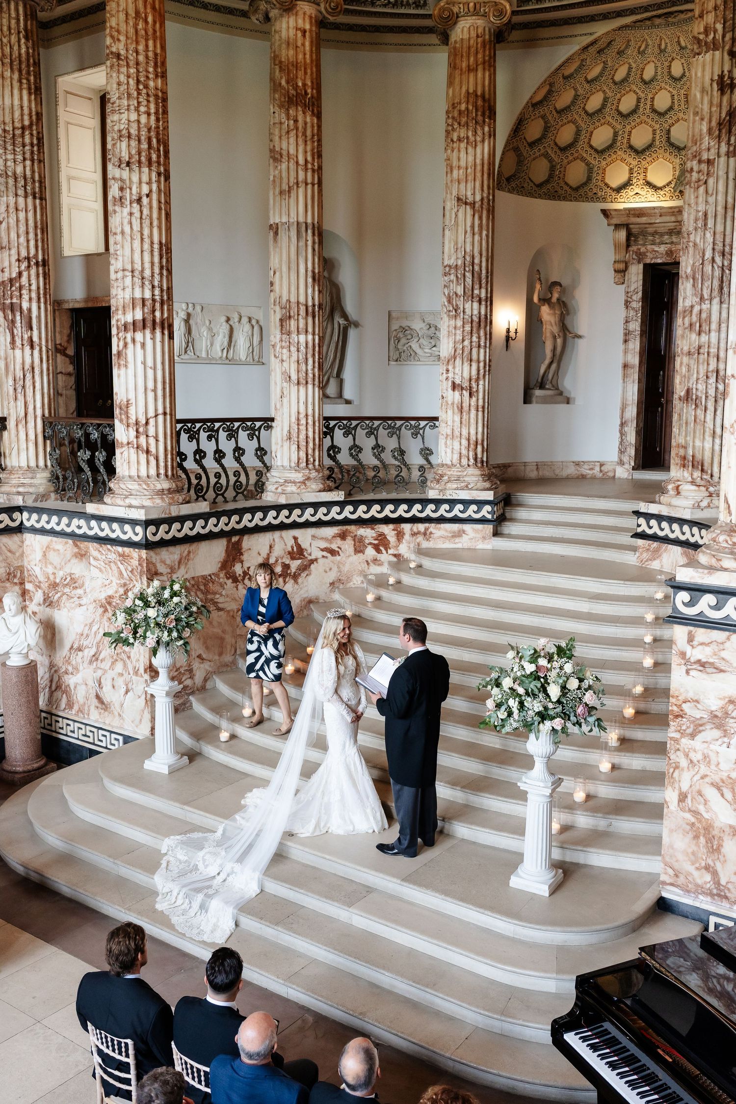 Bride and groom exchange vows at base of ornate marble staircase in stunning historic mansion.