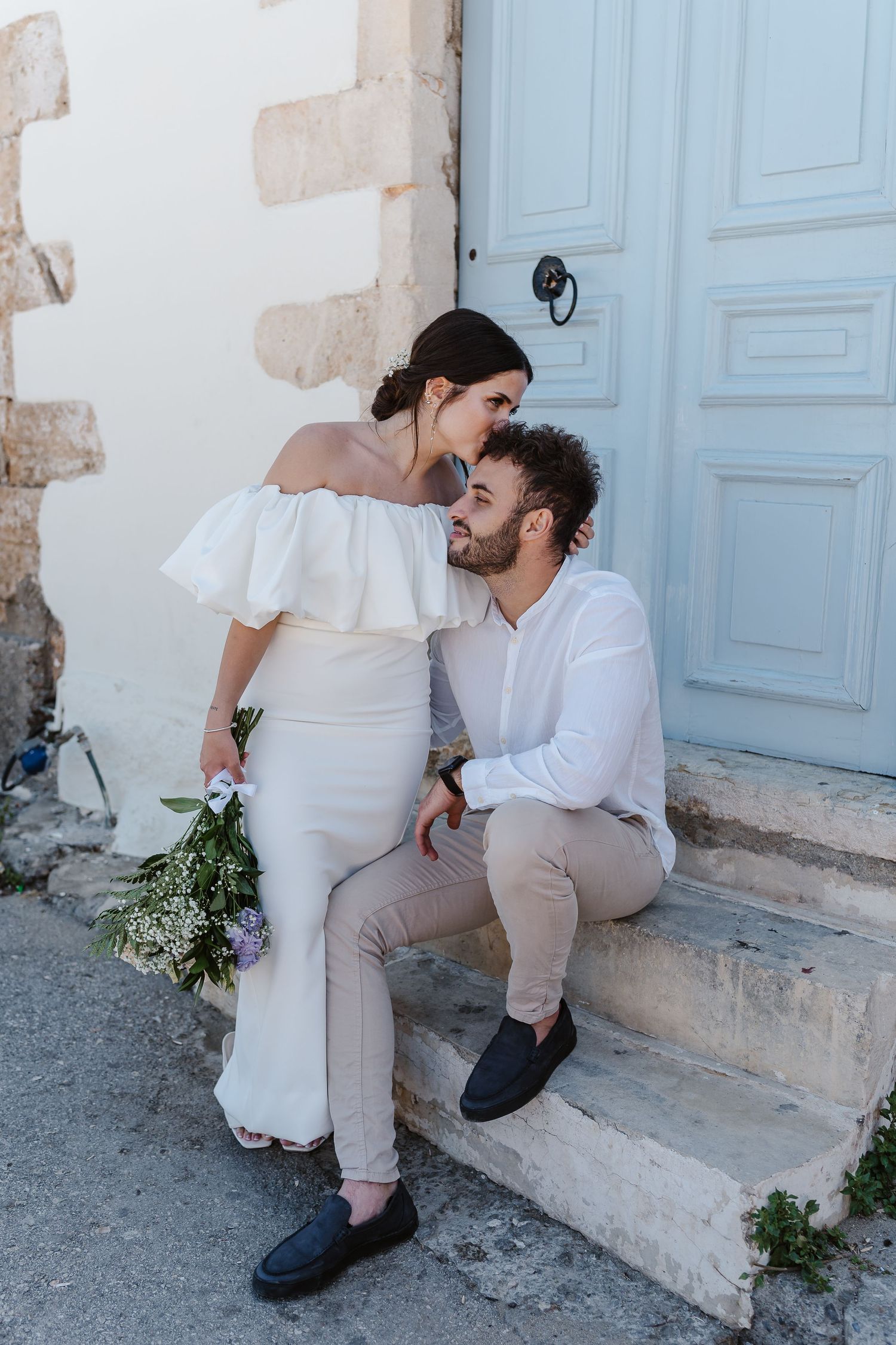 Couple in wedding attire gaze romantically at each other on rustic stone steps outdoors.
