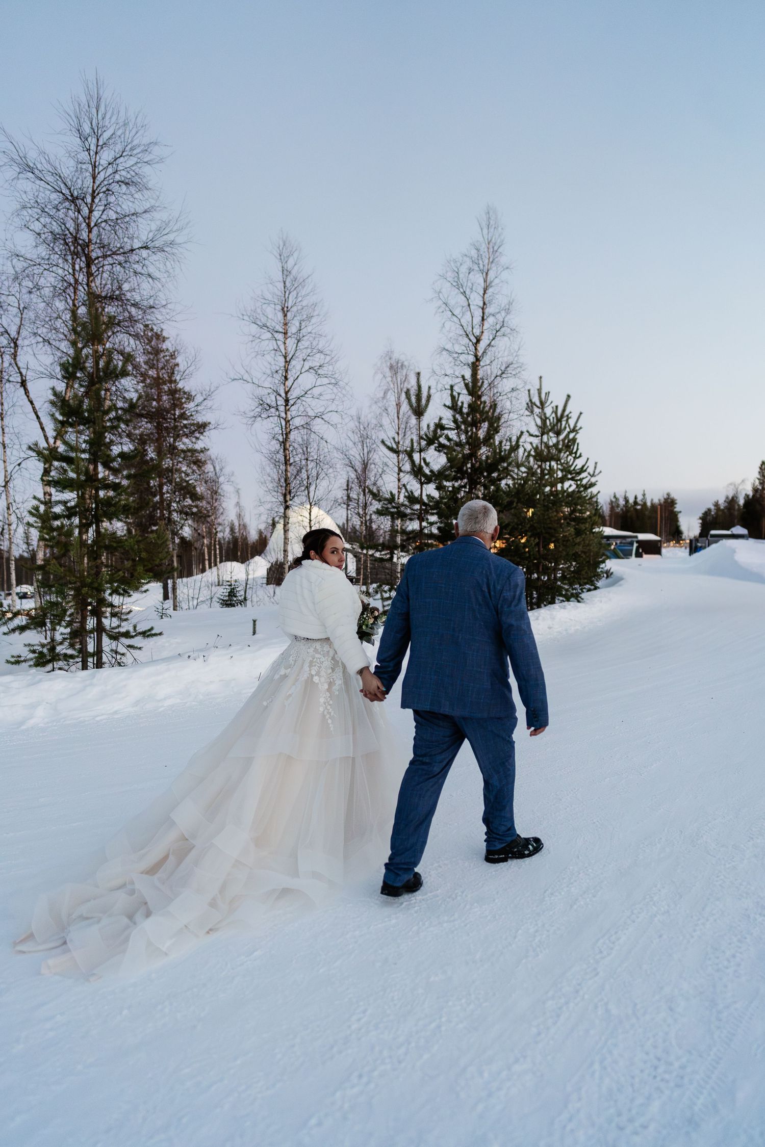 Couple candidly walking through forest with pink skies. Luxury Lapland wedding photographer. Snow wedding. Mountain Wedding.