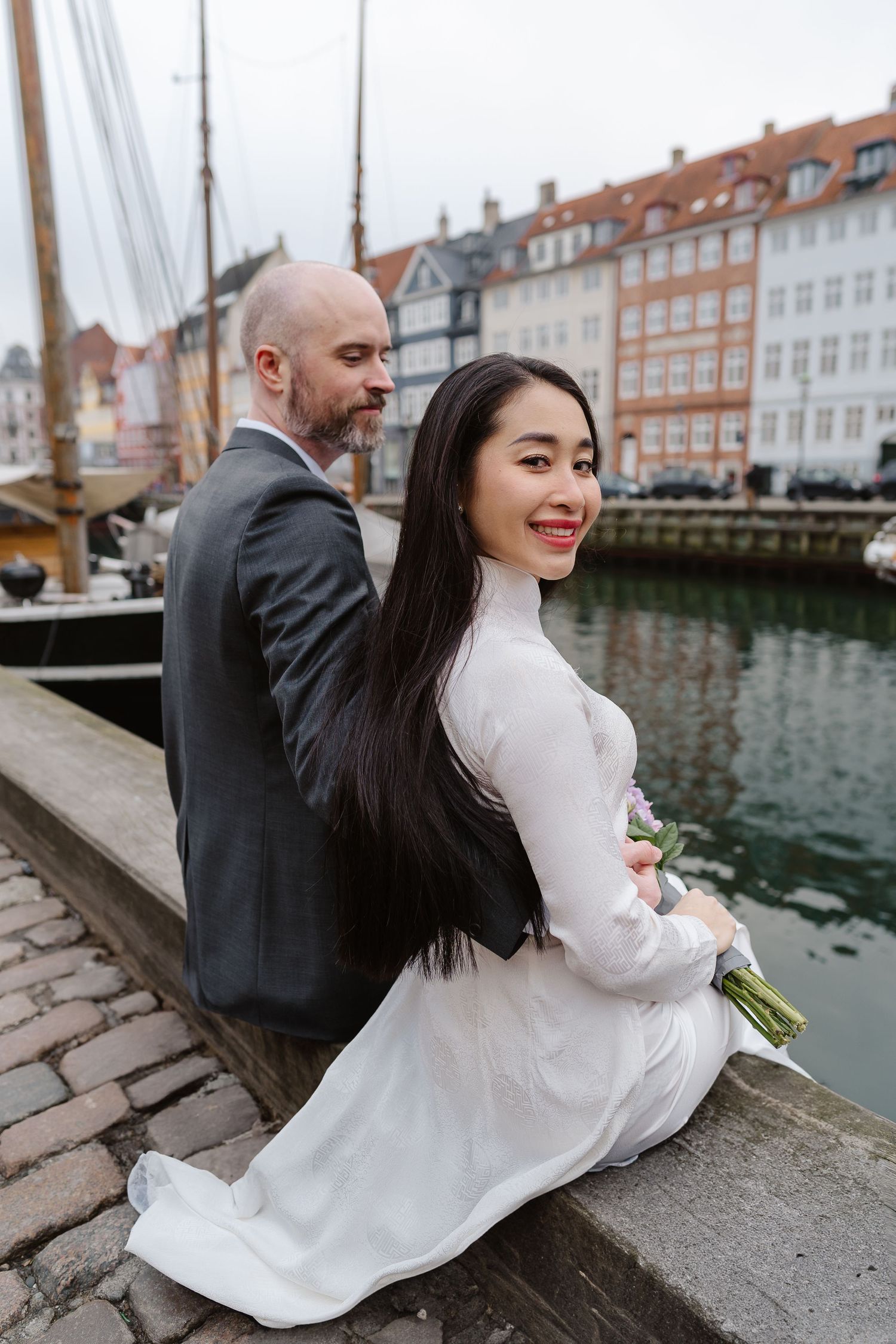 Newlyweds sitting along Nyhavn Canal in Copenhagen. Denmark wedding. Scandinavian & Destination Wedding Photographer