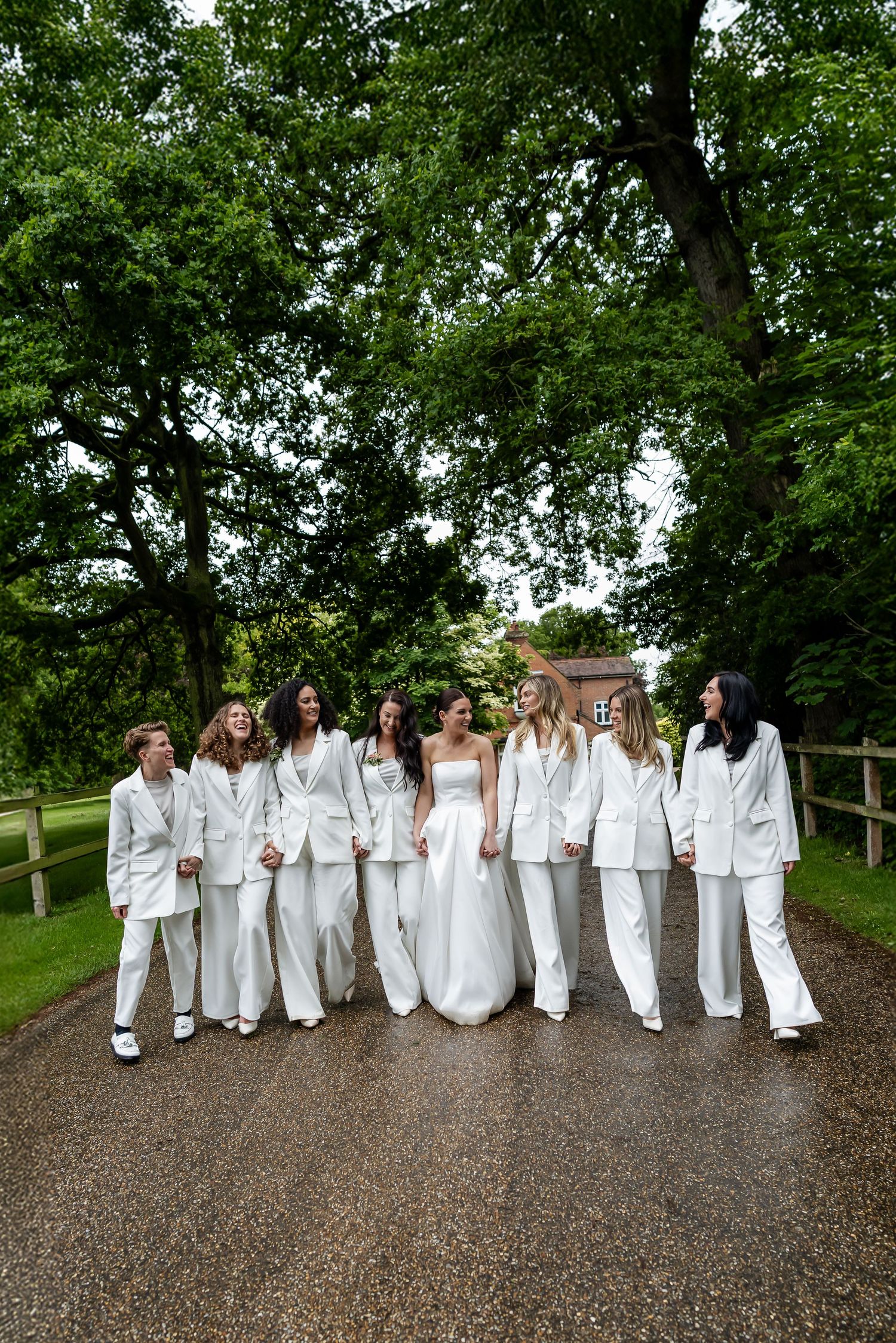 Bride with bridesmaids all dressed in white suits walking along scenic outdoor pathway.