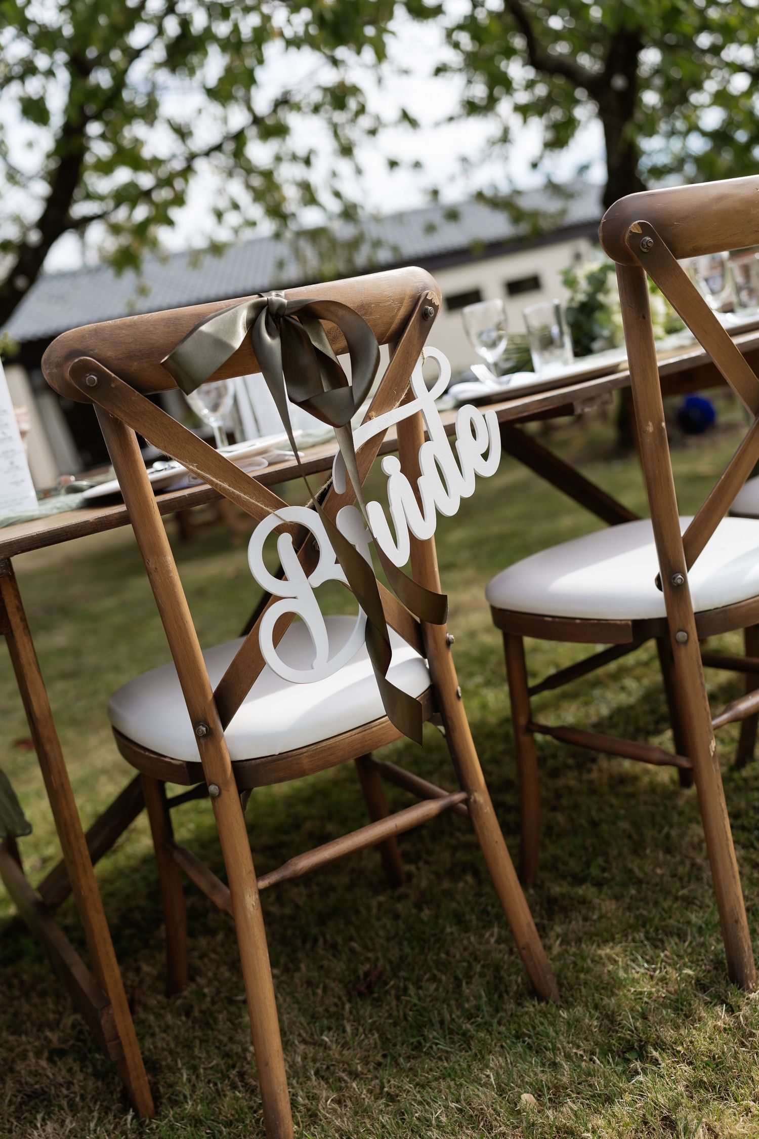 Wooden crossback chair with decorative white Bride sign at an outdoor wedding reception.