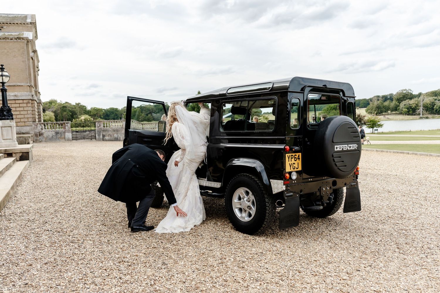 Bride and groom exiting a black Land Rover Defender at an elegant wedding venue on a gravel driveway.