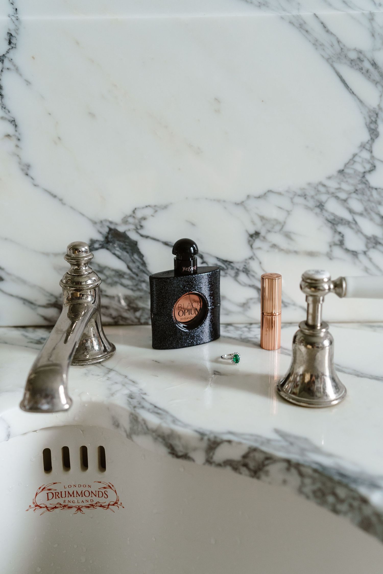 YSL Black Opium perfume and lipstick displayed on elegant marble bathroom sink.