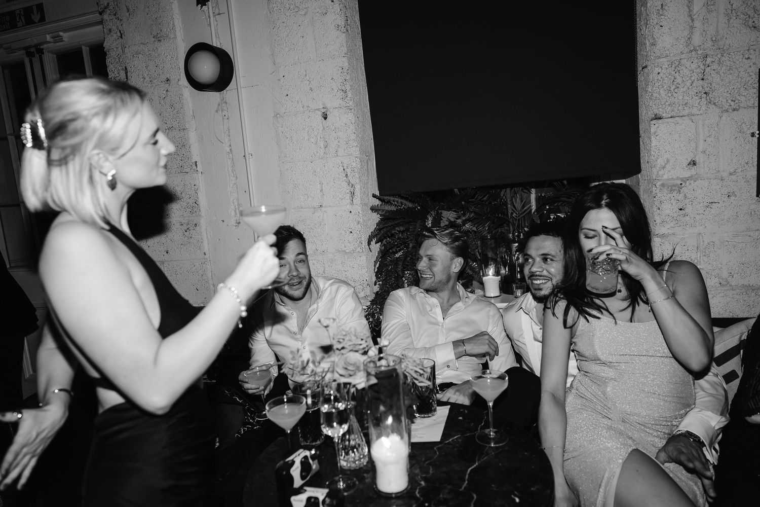 Black and white candid photo of wedding guests laughing and socialising at a reception party at London's cool wedding venue - the Kindred