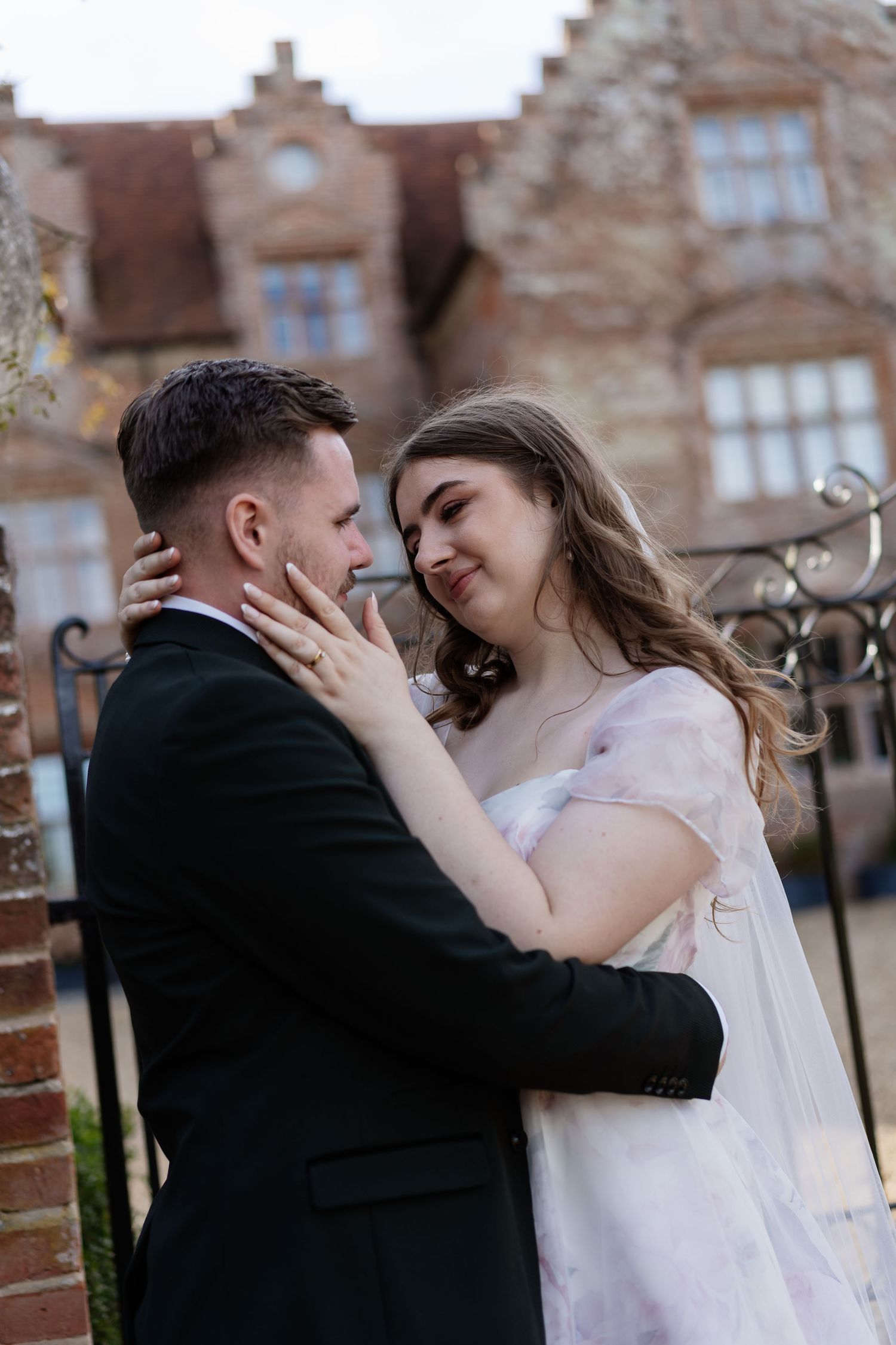 Bride and groom share a romantic embrace outside a historic brick building on their wedding day.