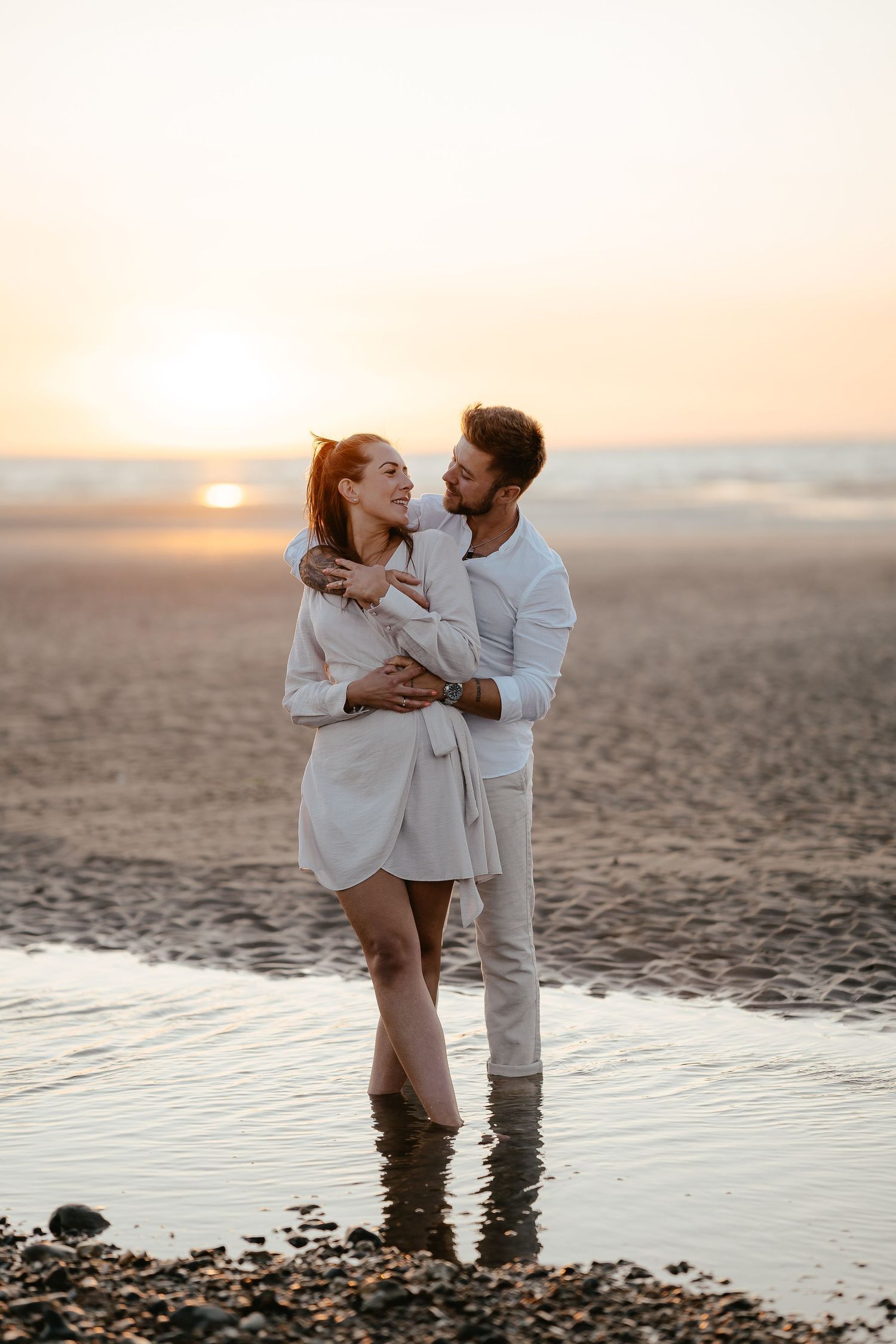 A happy couple sharing a romantic moment standing in shallow beach water during a beautiful sunset.