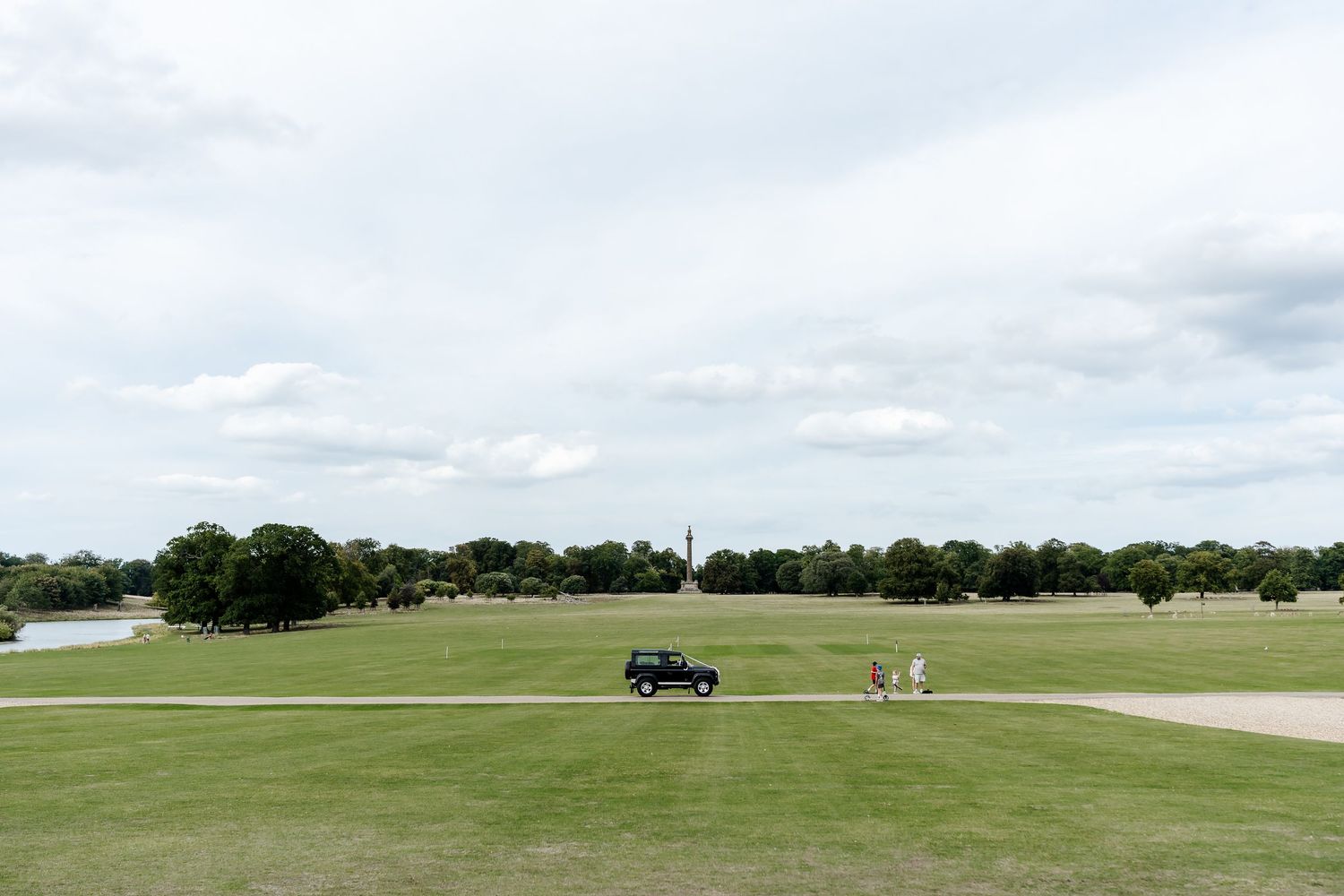 A golf course with a black car and players on a lush green fairway under a cloudy sky.