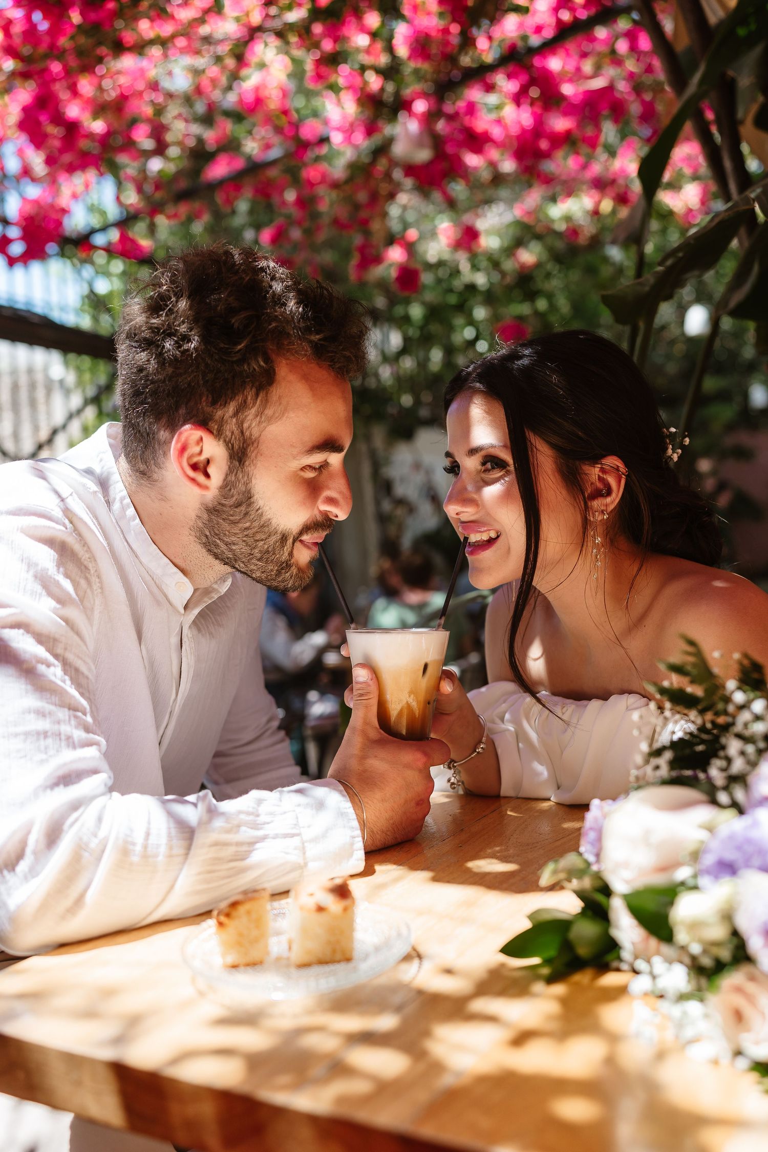 Romantic couple gazing at each other over an iced latte under colorful pink flowering bougainvillea.