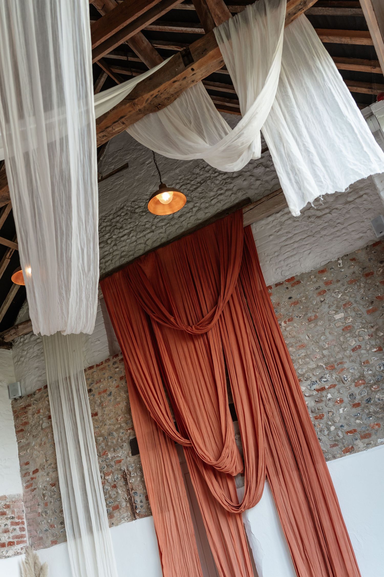 Rustic wedding venue interior with draped terracotta and white fabric hanging from a wooden ceiling.
