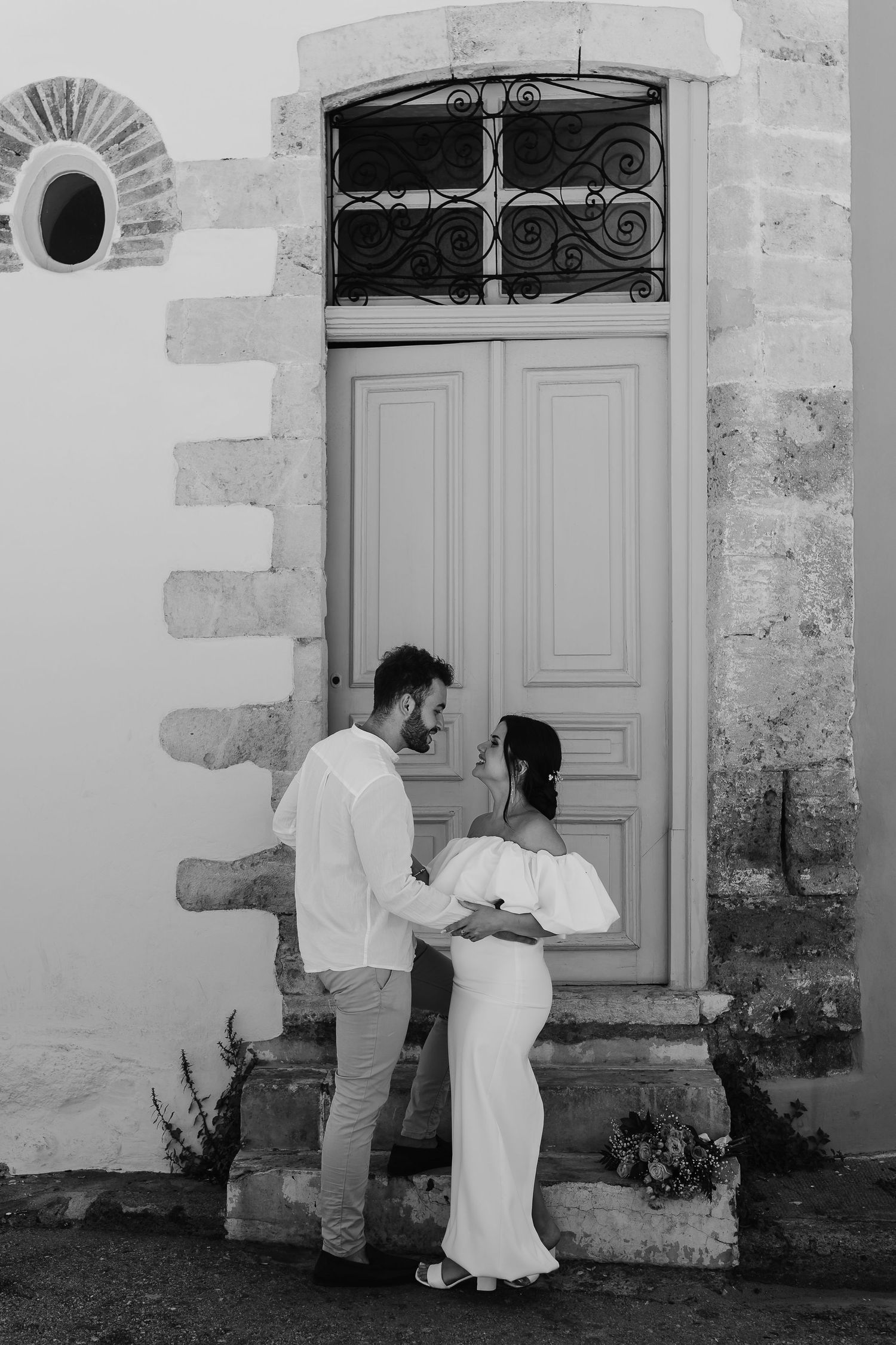 Black and white photo of bride and groom embracing tenderly before an ornate vintage doorway.