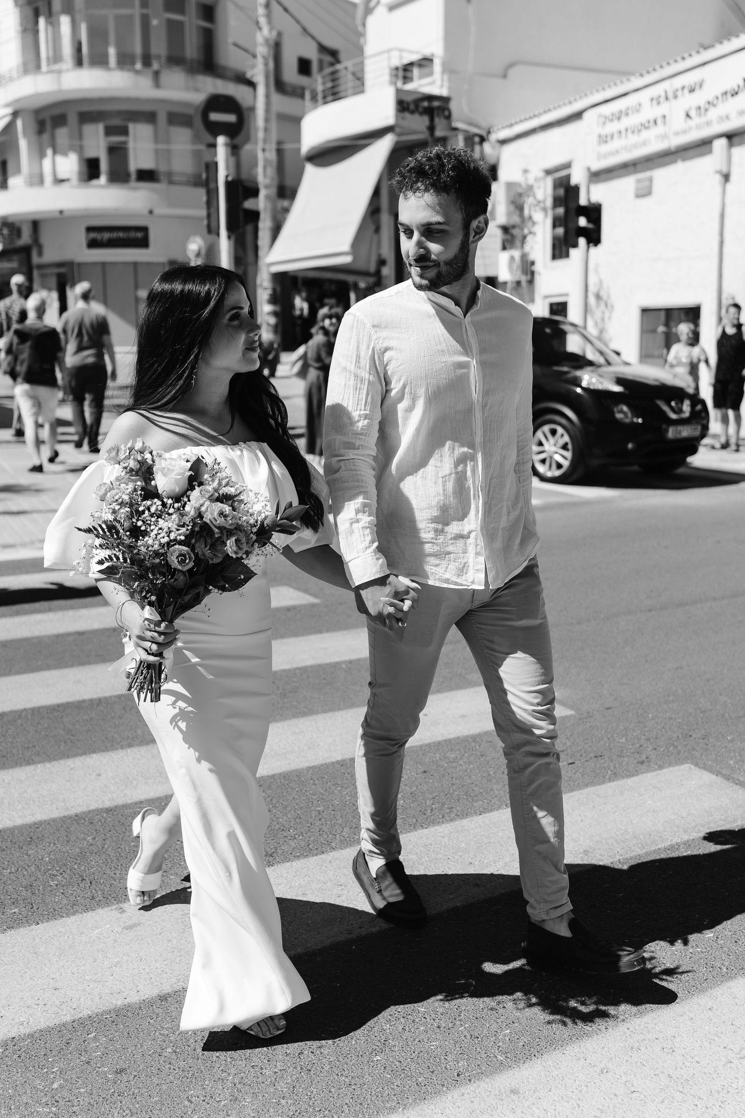 Black and white photo of bride and groom crossing a zebra crossing in a busy city street.