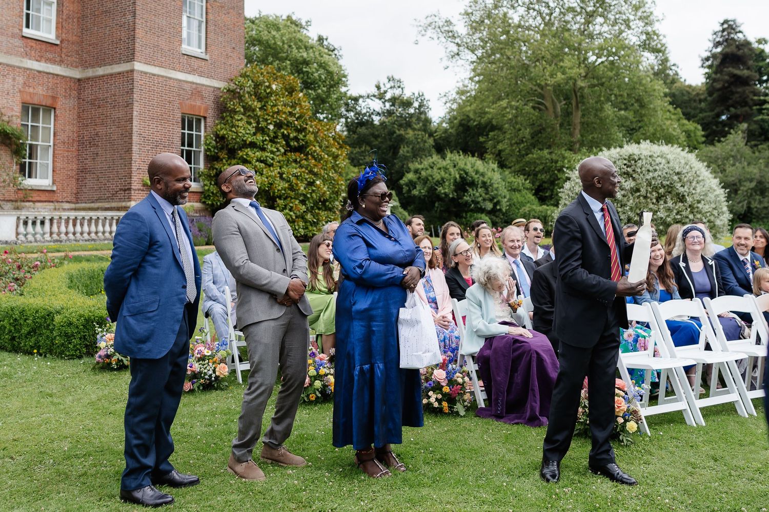 Wedding guests standing and celebrating during outdoor ceremony on sunny day at historic brick estate.