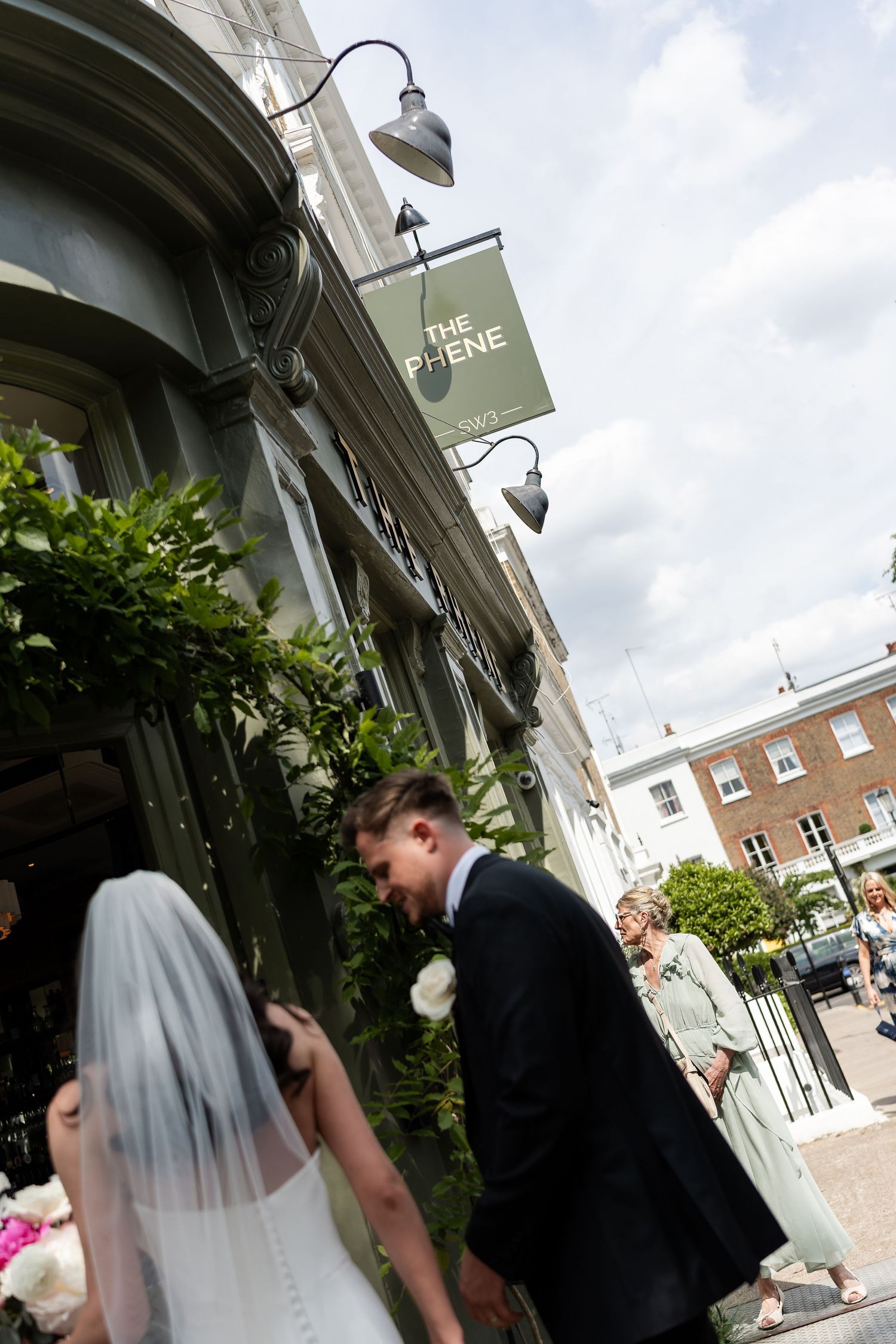 Bride and groom enter The Phene pub venue in Chelsea on bright summer wedding day.