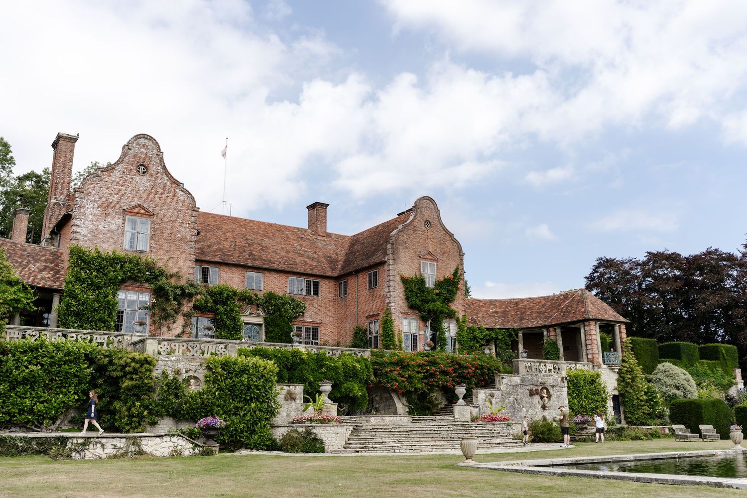 Historic red brick English manor house wedding venue surrounded by lush gardens under cloudy sky.