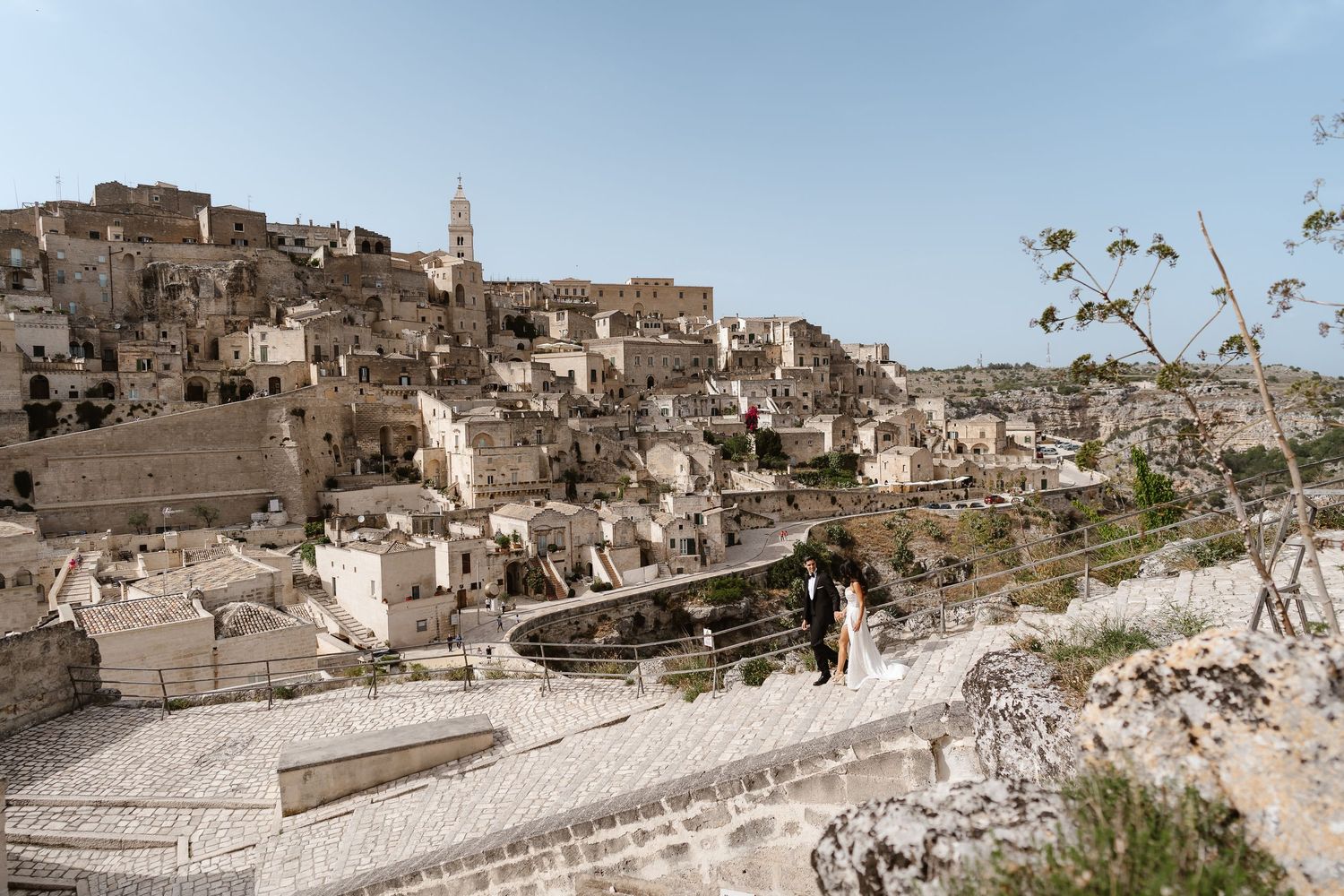 Couple exploring ancient stone city of Matera, Italy, with dramatic UNESCO heritage site panorama.