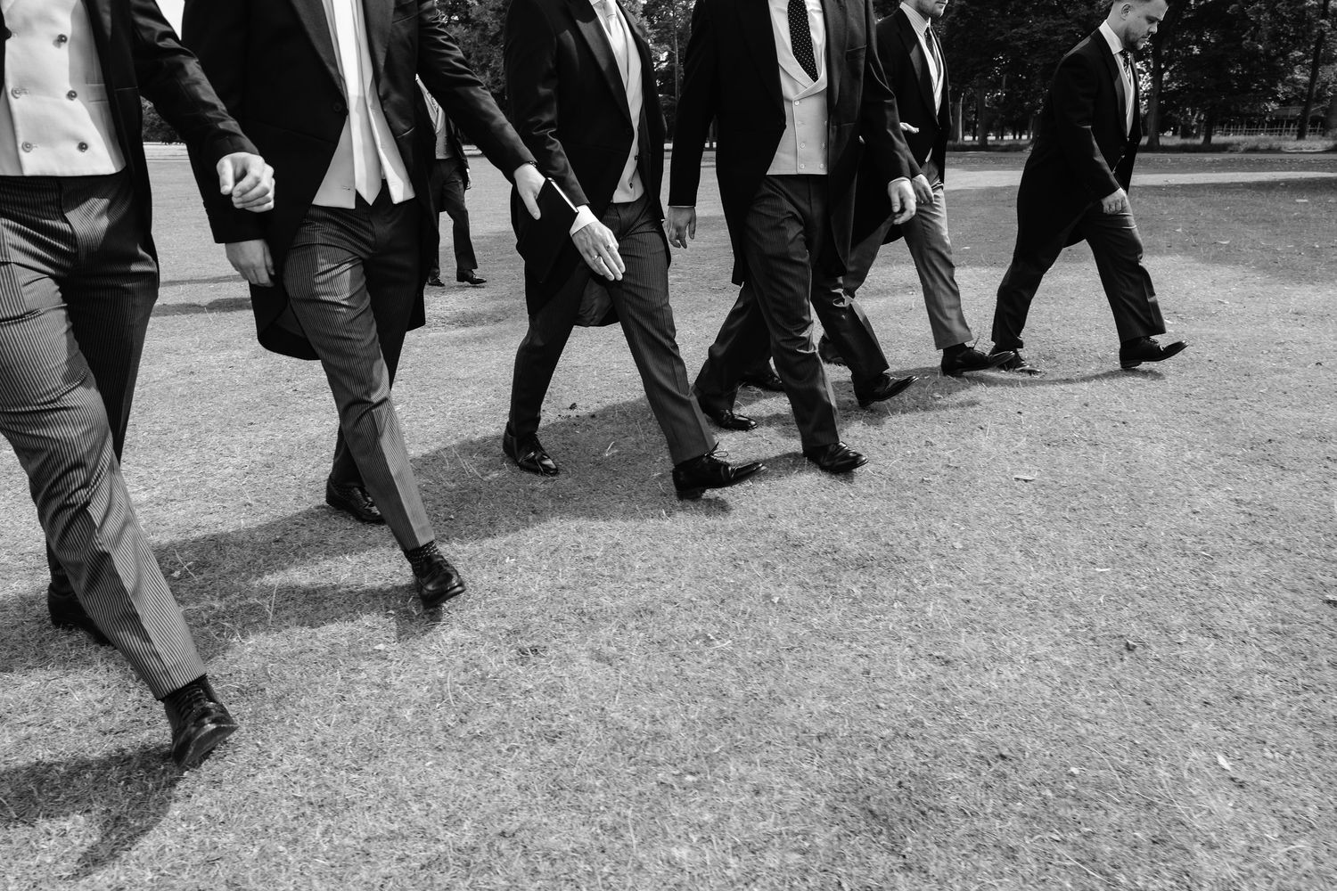 Black and white photo of groomsmen in suits walking together on a path at a wedding.