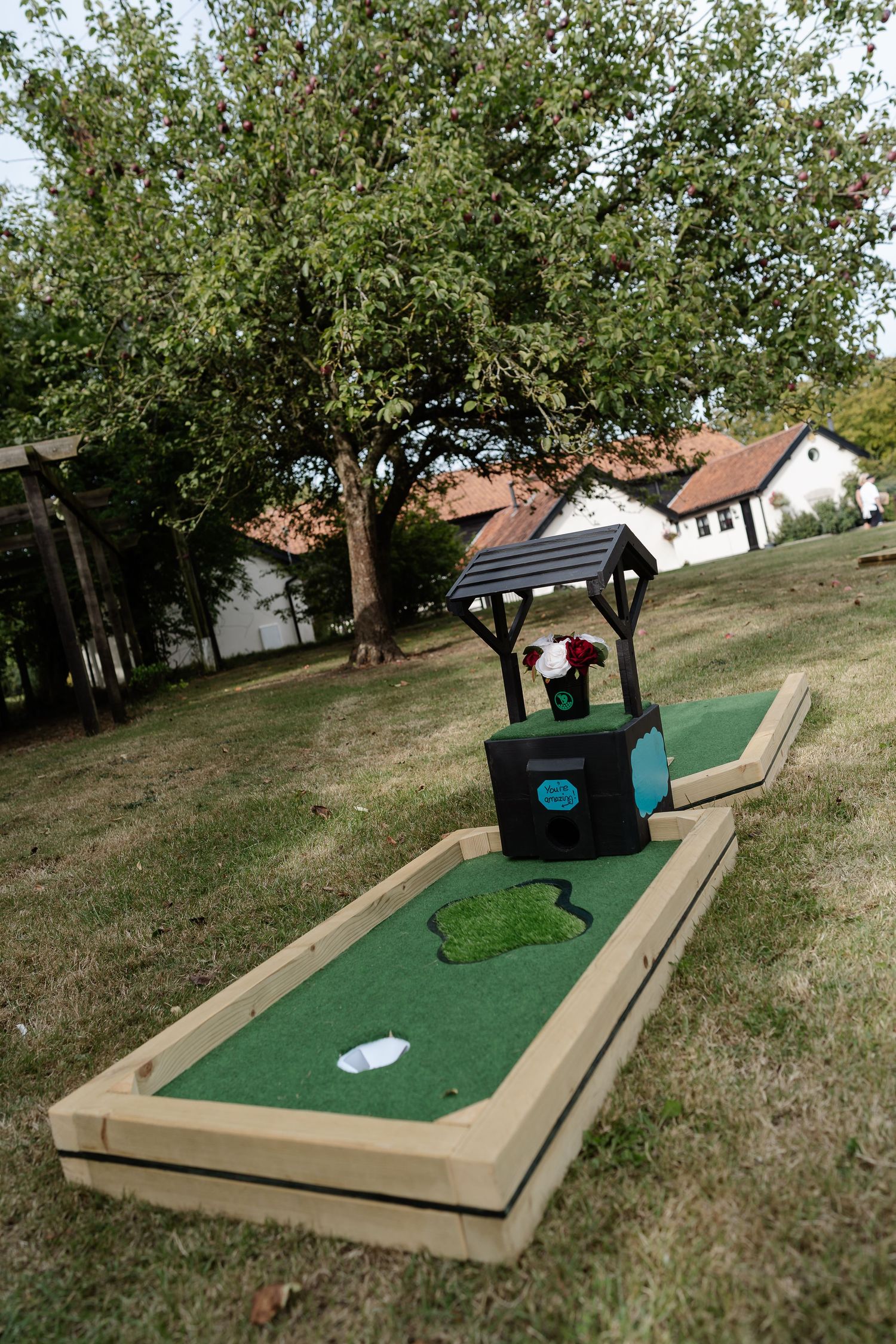 Custom mini golf hole with wishing well obstacle set up on green grass for outdoor wedding entertainment.