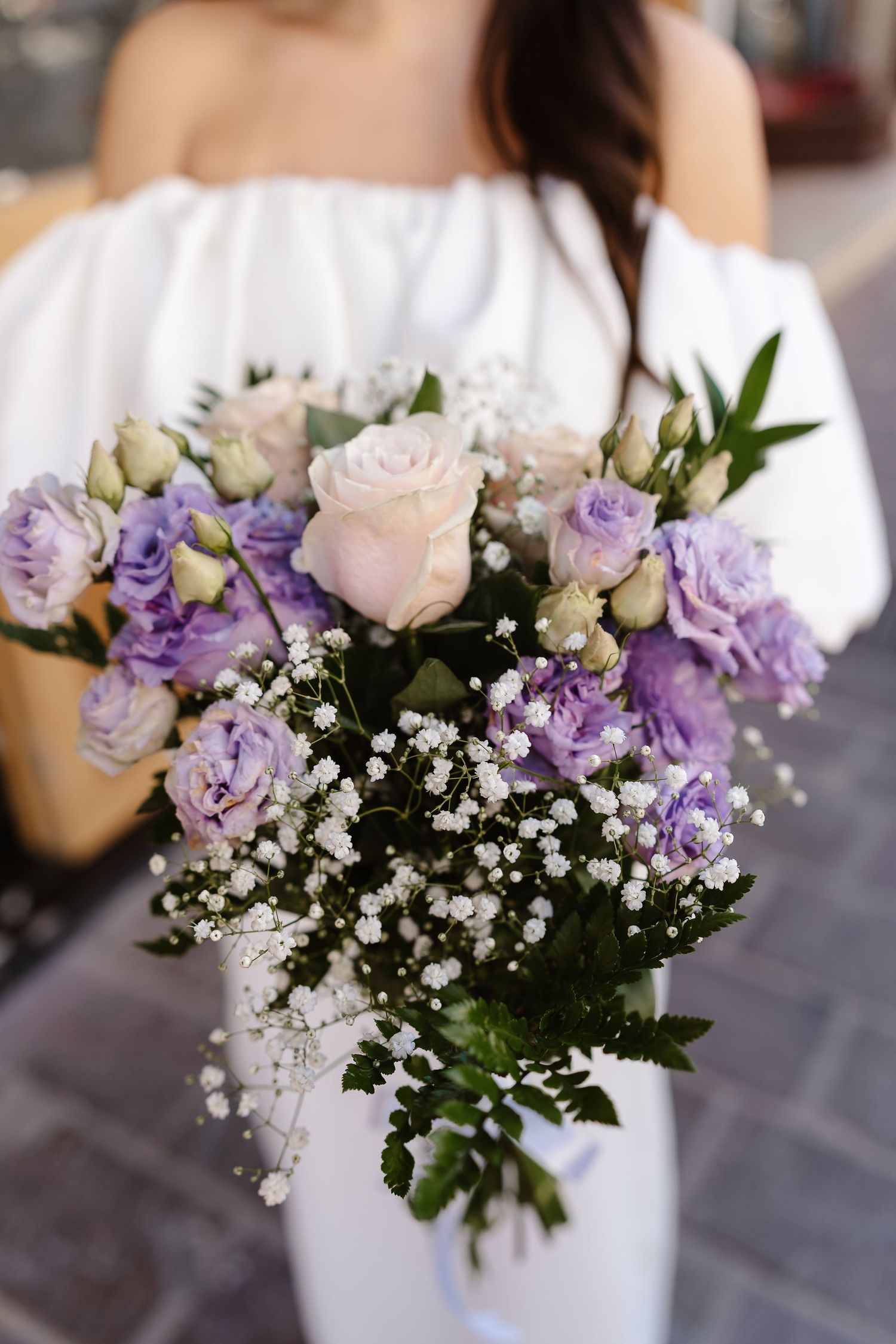 Close-up of a bridal bouquet featuring purple lisianthus, pink roses, and delicate white gypsophila.