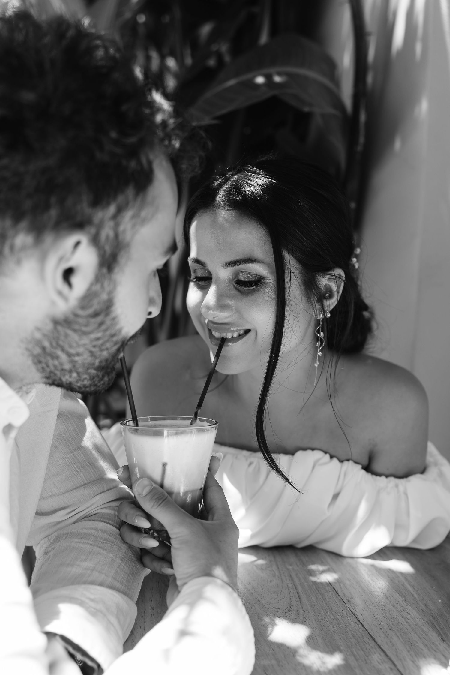 Black and white photo of bride sipping a milkshake while sharing an intimate moment with groom.