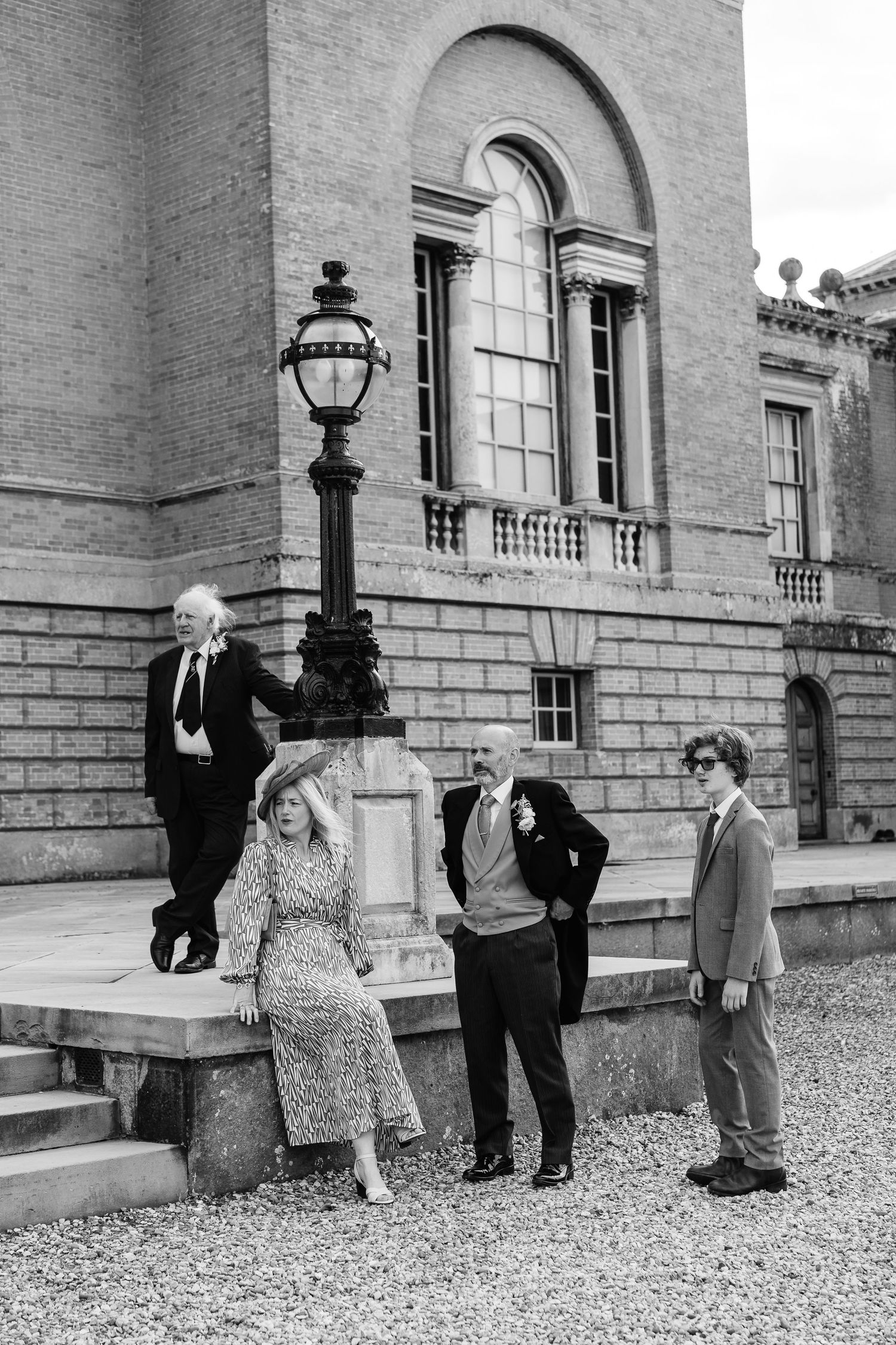 Wedding guests posing by a lamppost outside a grand historic brick building.