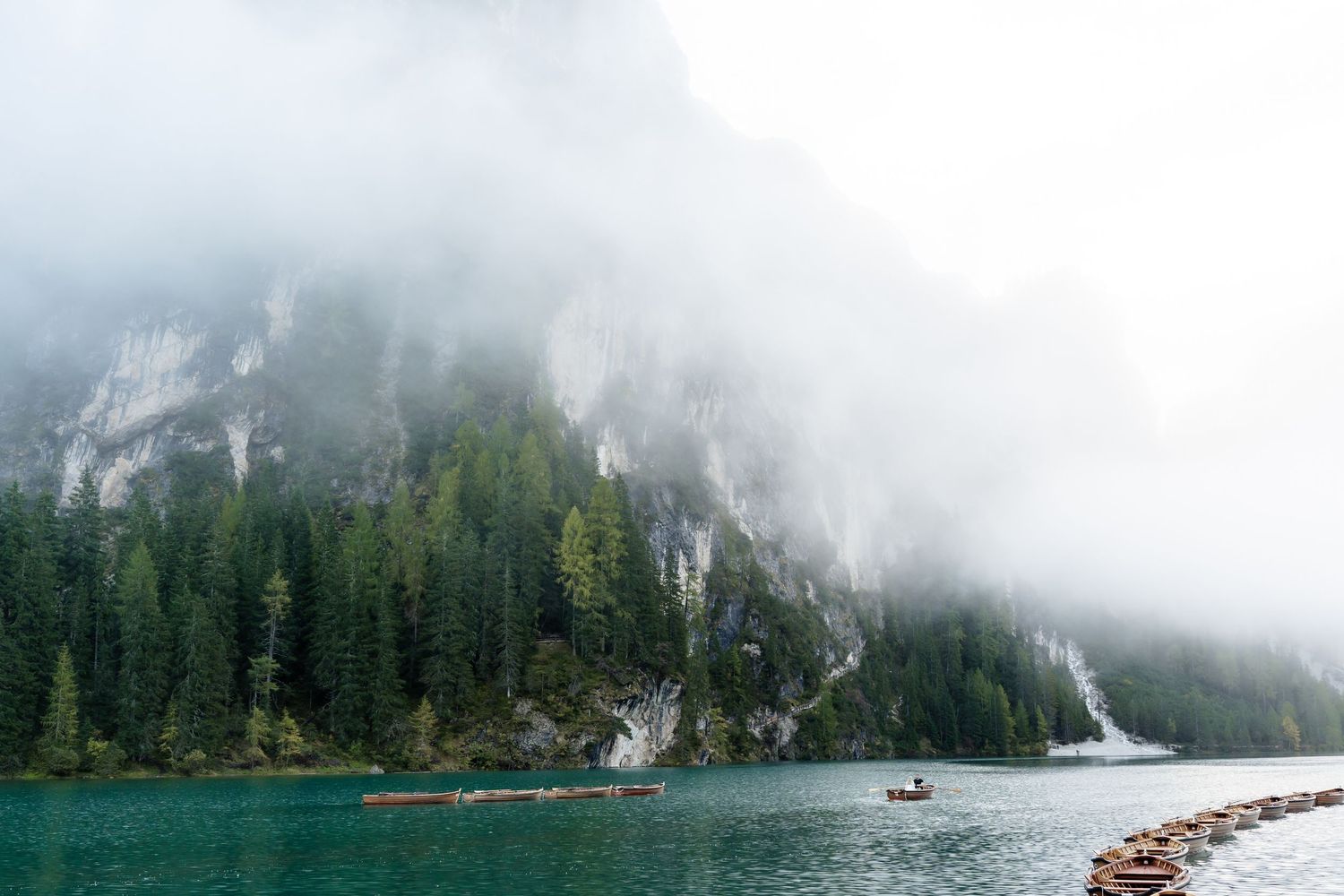 Misty mountain lake Lago di Braies in Dolomites with eloping couple on a row boat and incredible scenery for magical elopement photography