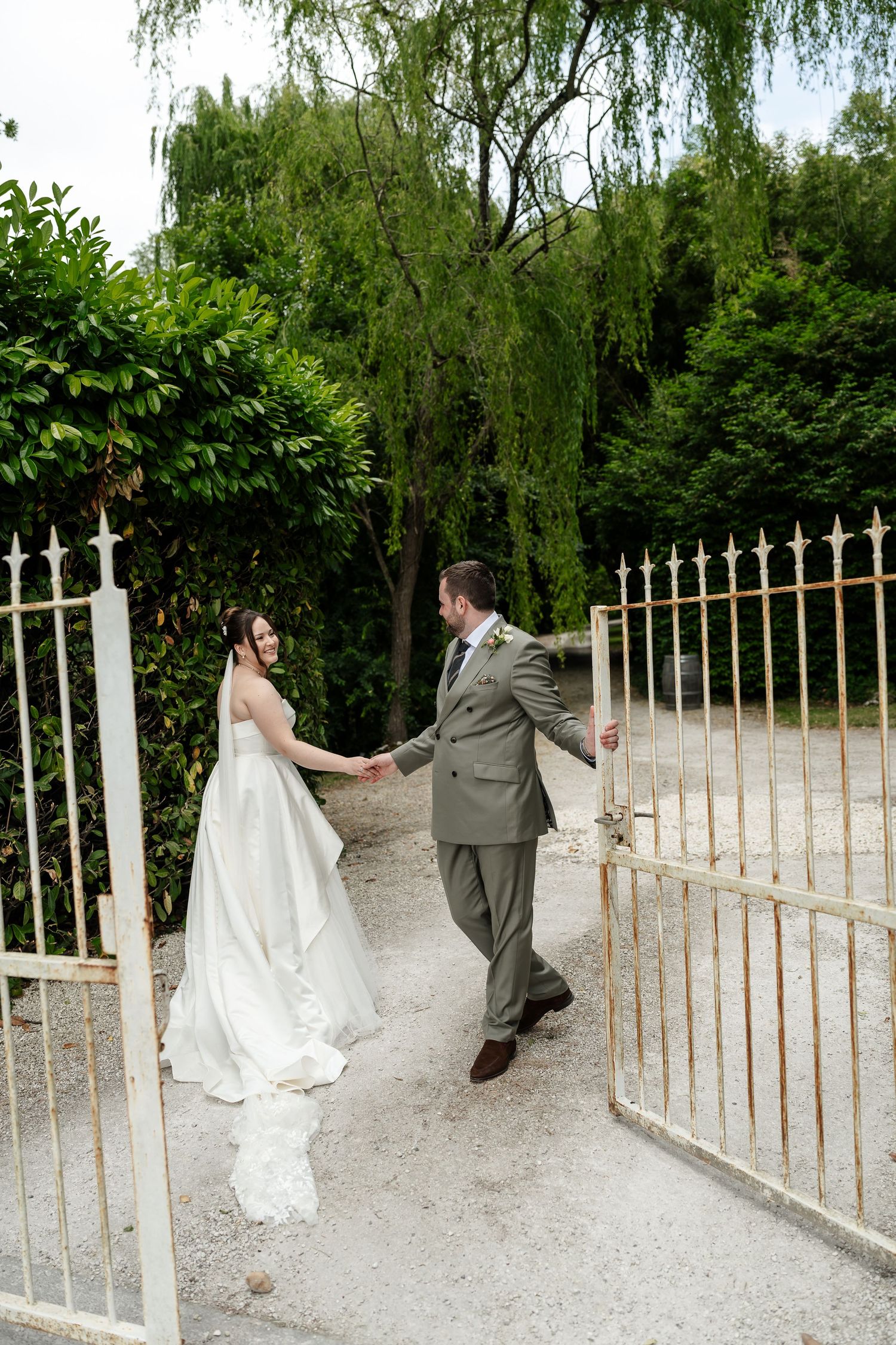 Bride and groom holding hands at golden gates surrounded by lush greenery on their wedding day.
