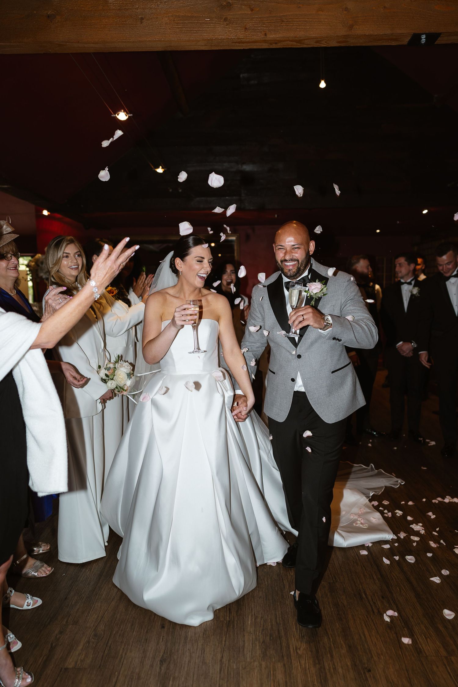 Bride and groom walk through flower petal confetti shower during joyful wedding reception entrance.