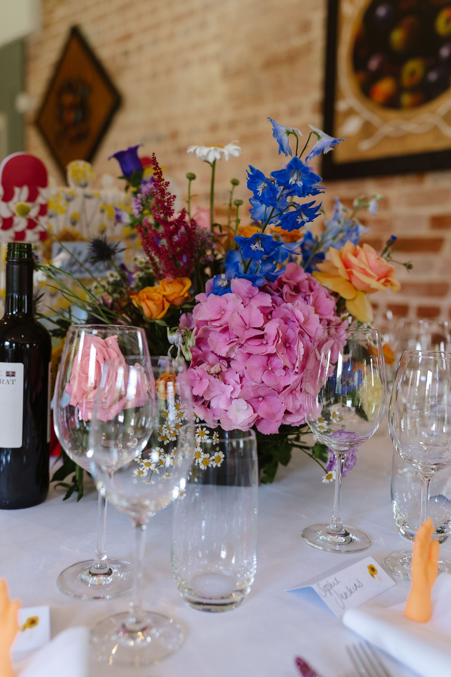 Vibrant wedding table centerpiece featuring pink hydrangeas, blue delphiniums, and wine glasses.