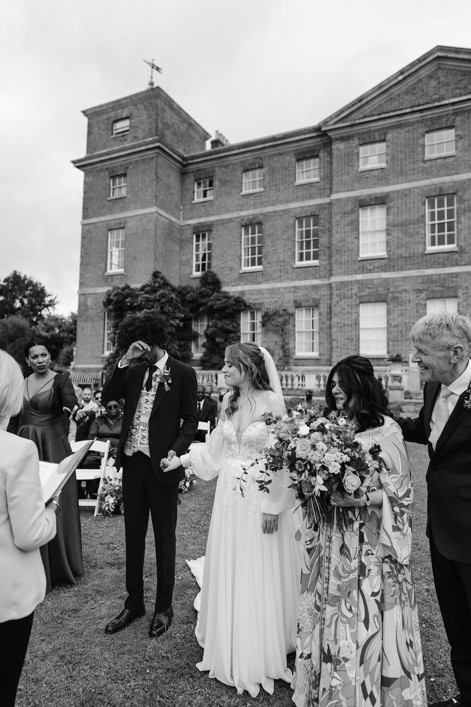 Black and white photo of bride and groom during outdoor wedding ceremony at historic brick estate.