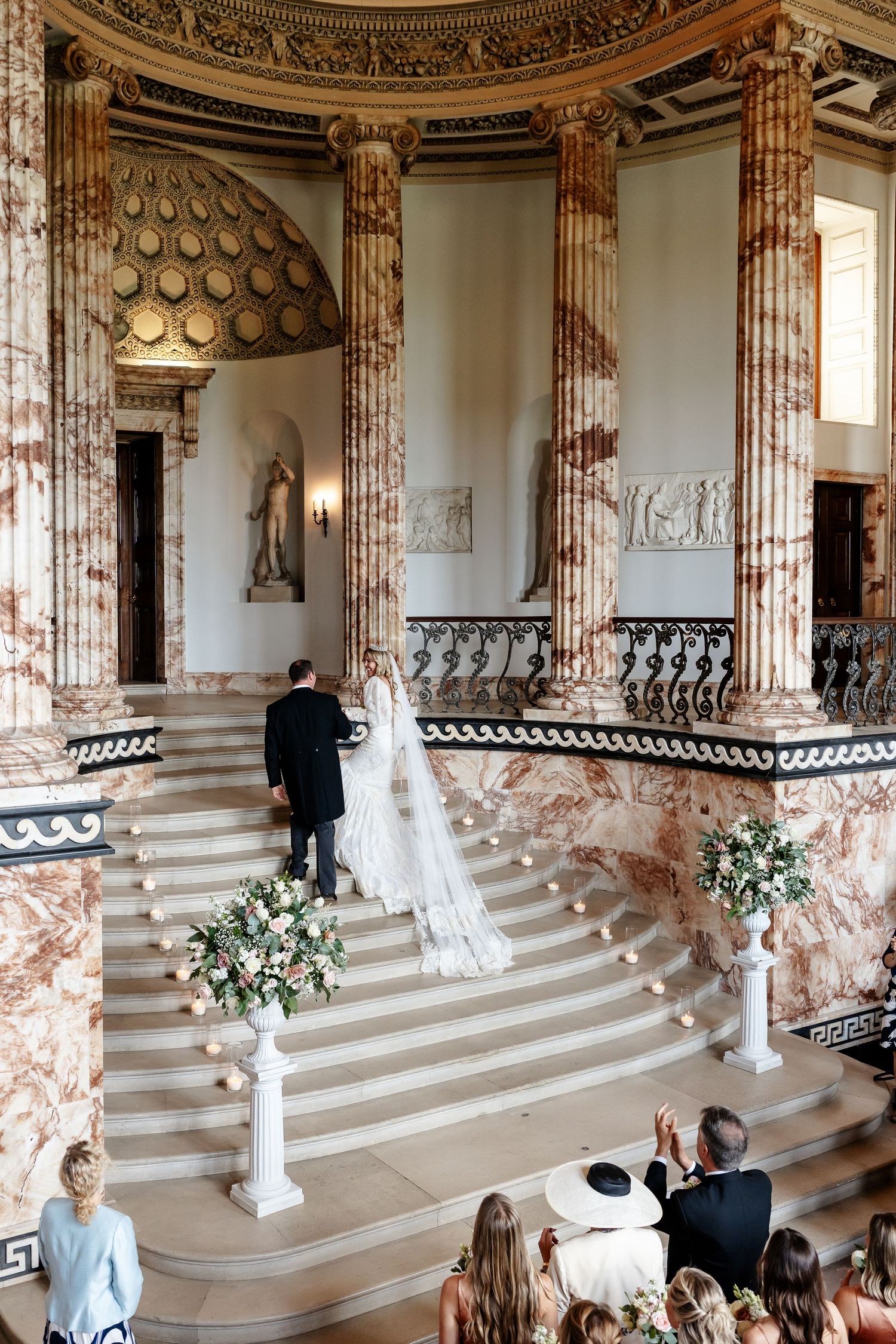 Bride and groom at the altar of a grand marble staircase in a stunning historic venue.