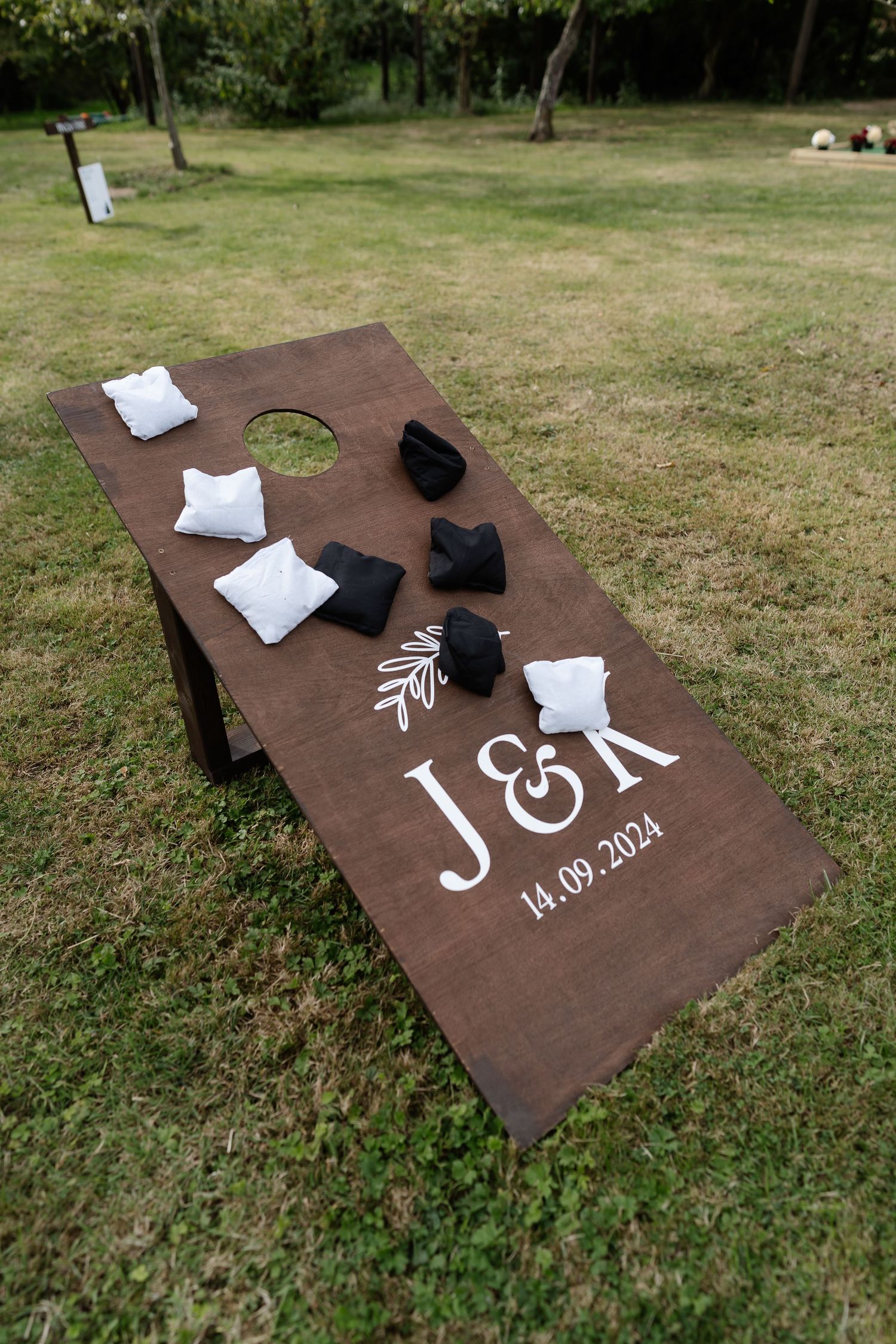 Custom cornhole board engraved with J&K wedding monogram and date 14.09.2024 with black and white bean bags.