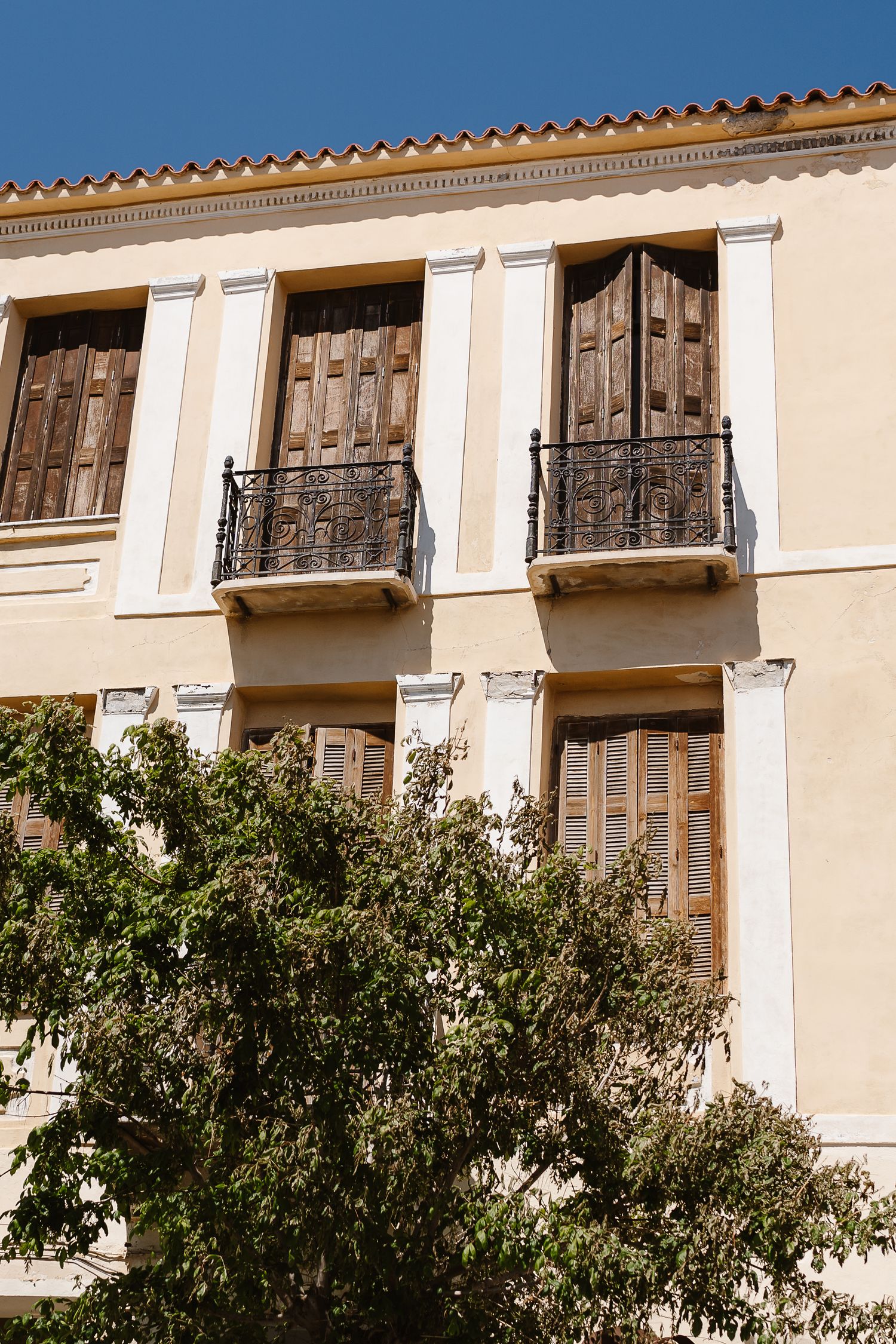 Neoclassical building facade with wooden shutters and wrought iron balconies in warm yellow stucco, Athens Greece.