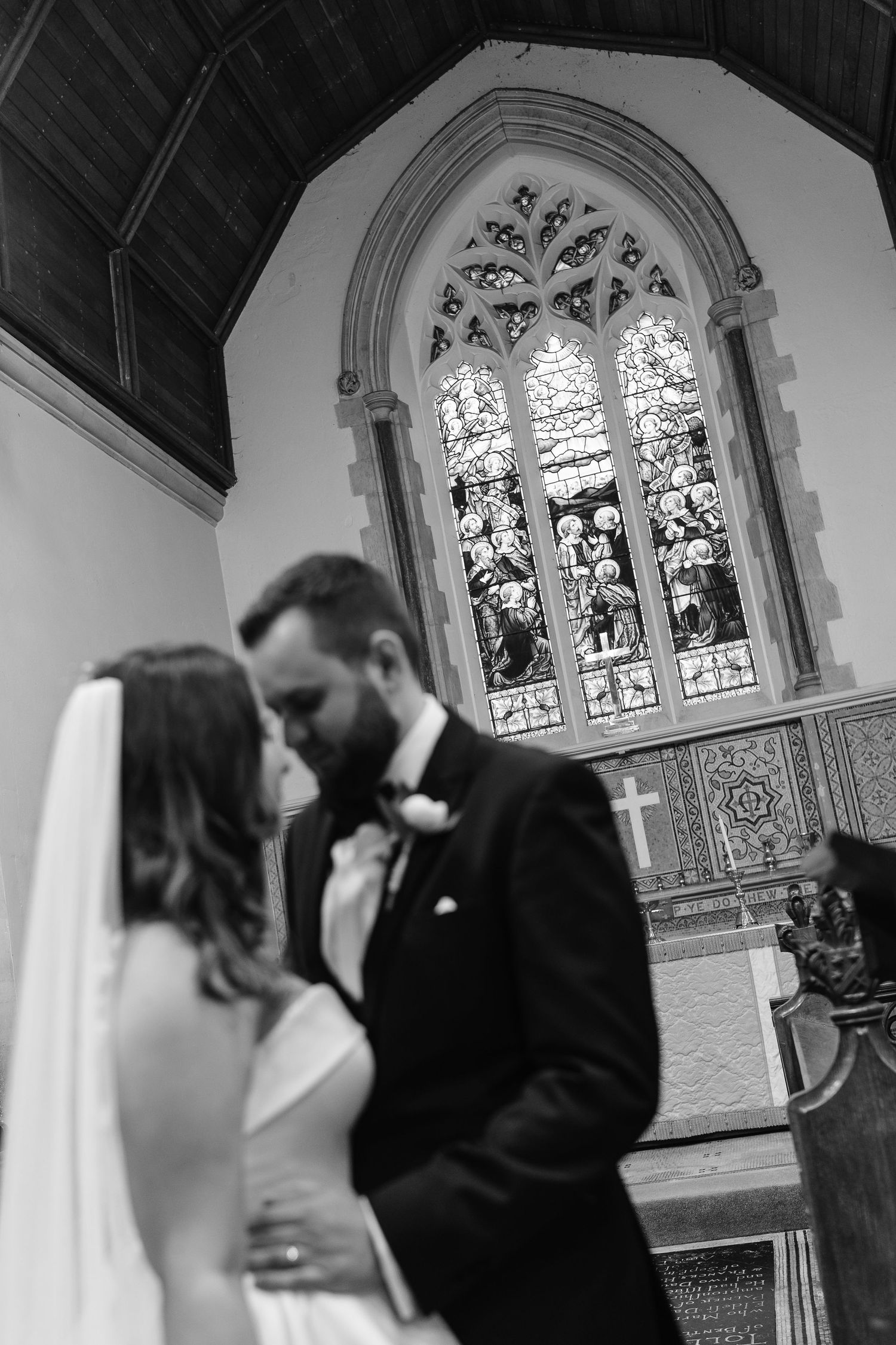 Intimate black and white portrait of bride and groom sharing a moment before stained glass church window.