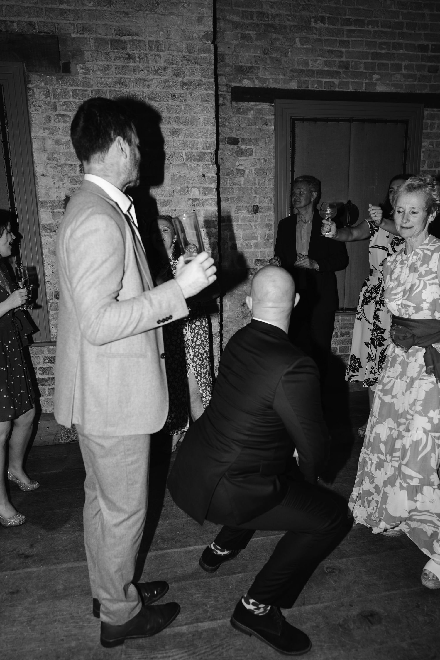 Black and white photo of wedding guests dancing energetically at a reception party.