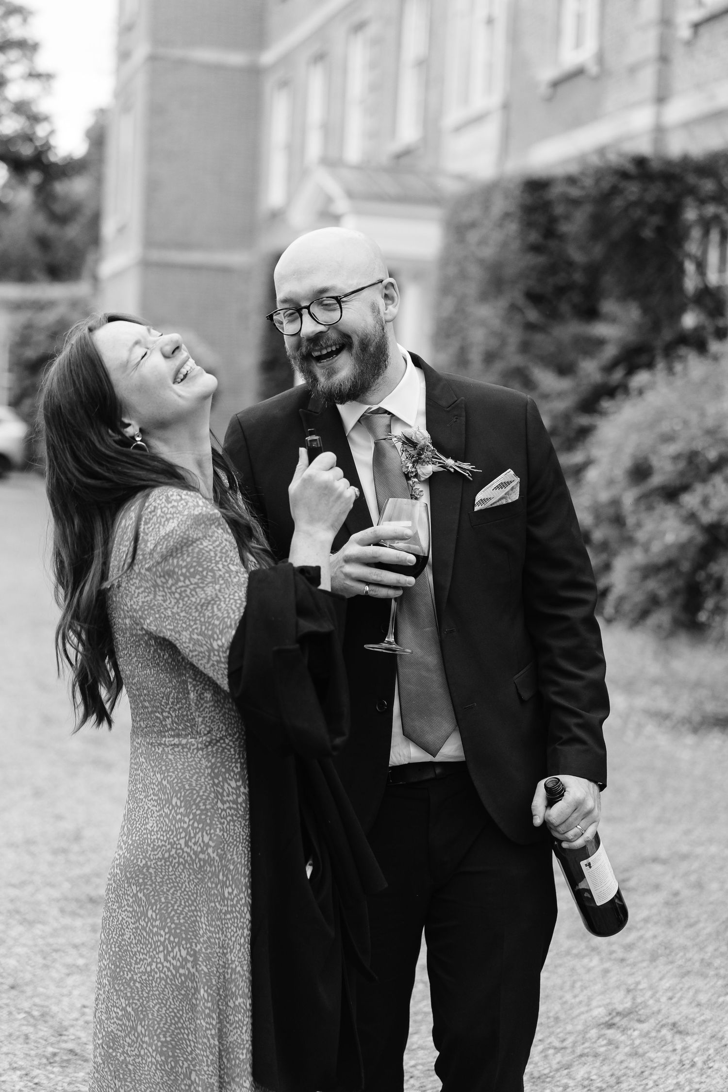 Black and white photo of laughing couple with champagne bottle at wedding.