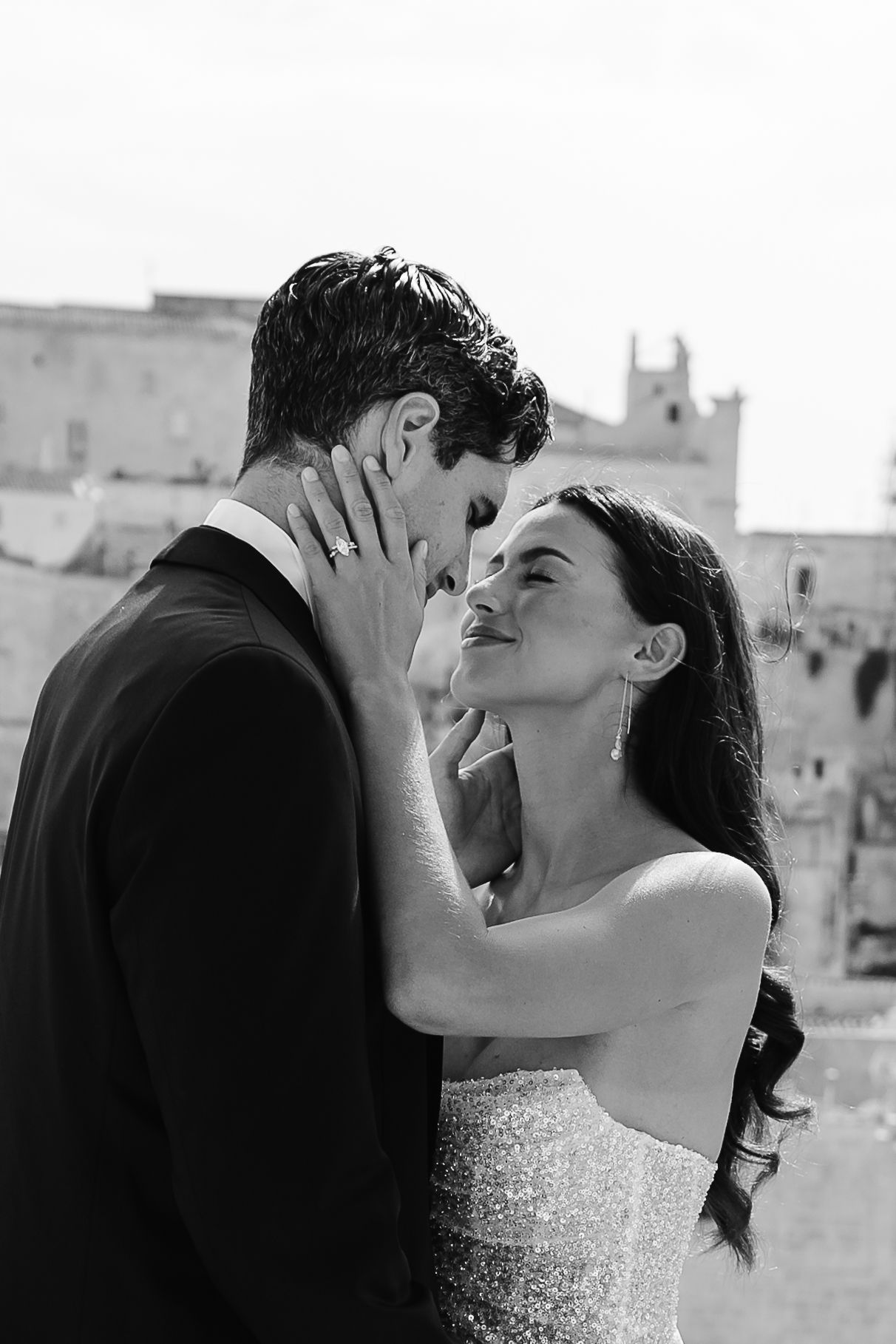 B&W Gentle tender hands touching the grooms face. Warm embrace in the Italian sunshine.