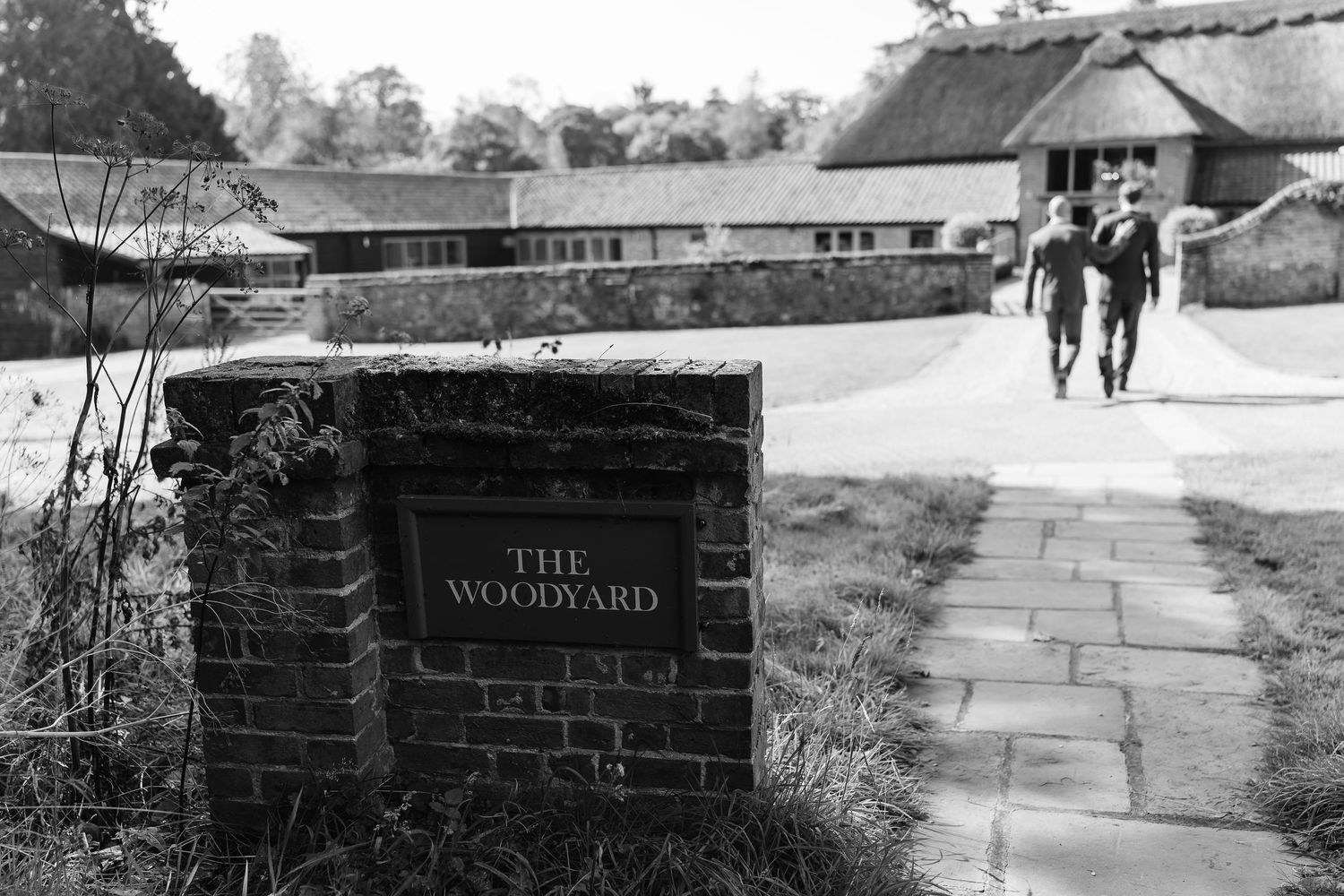 Black and white photo of The Woodyard venue entrance sign with guests walking along a path.