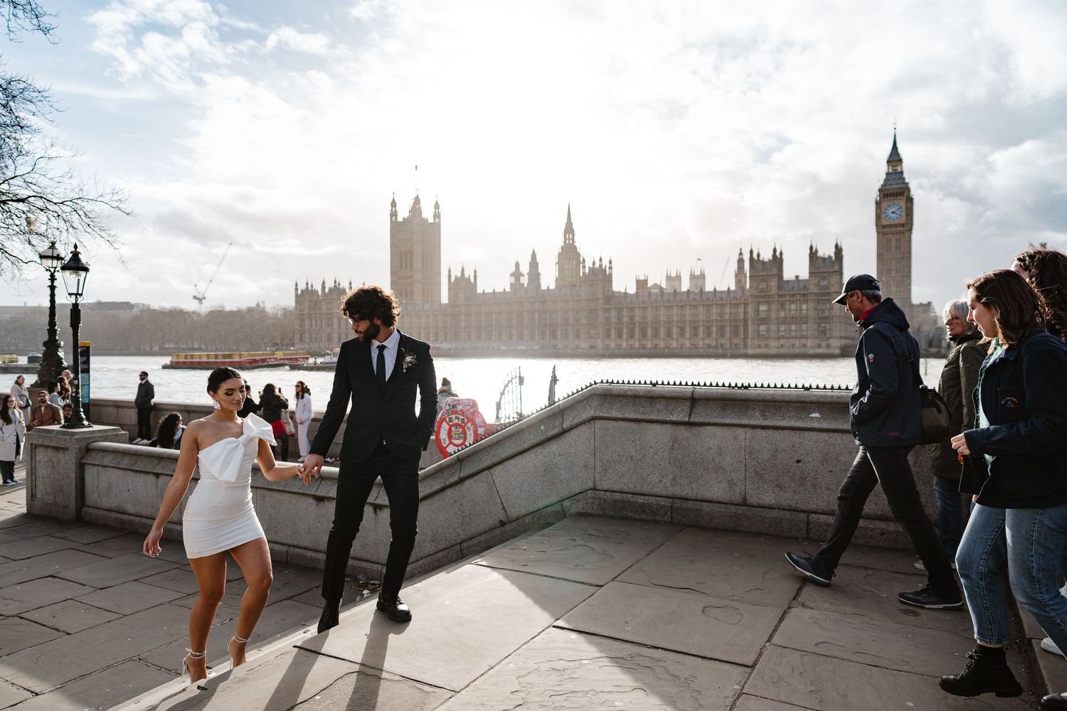 Bride and groom walking along the Thames with Big Ben and Houses of Parliament in the background, London.