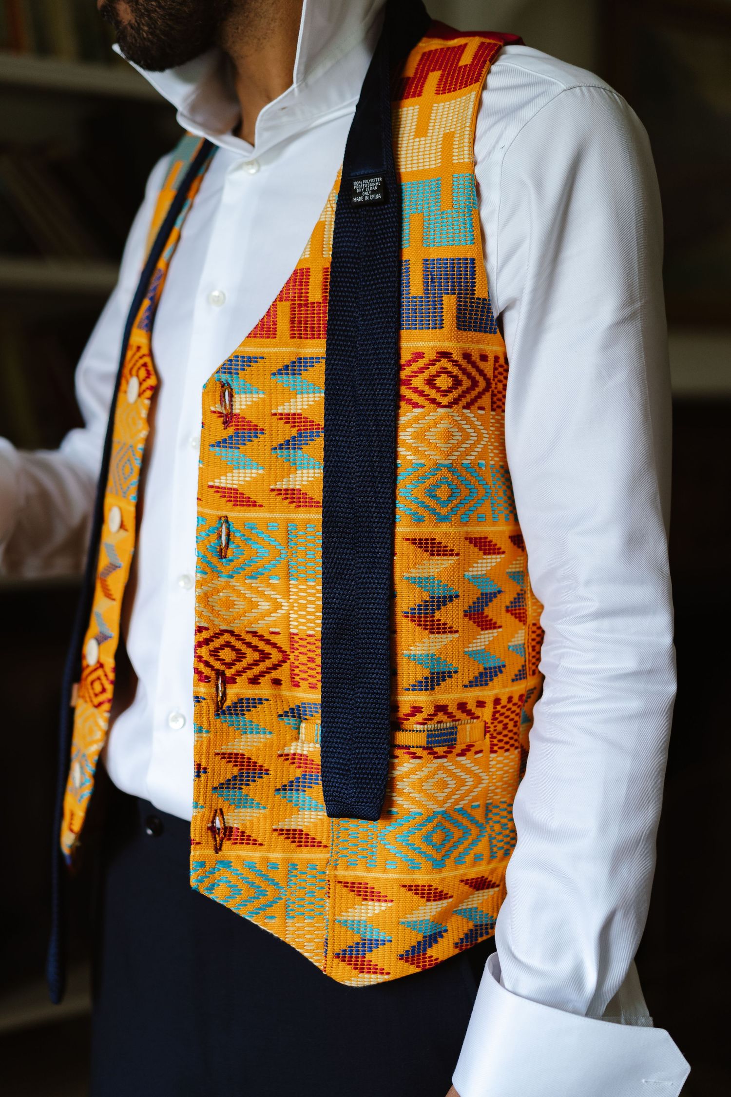 Close-up of groom wearing vibrant African Kente cloth vest with navy suit trousers.