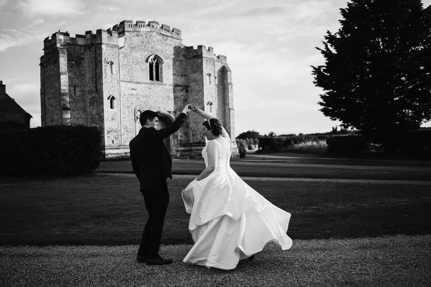 Black and white photo of bride and groom dancing elegantly in front of a medieval castle ruin.